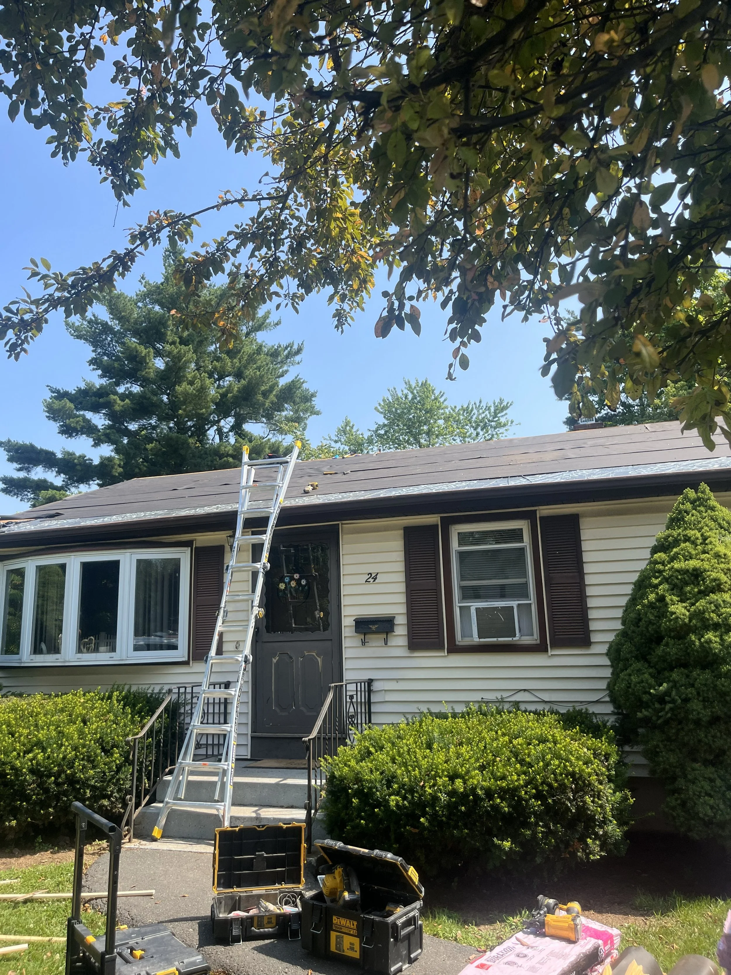 House with a ladder leaning against the roof and tools on the driveway, indicating roof repair work in progress.