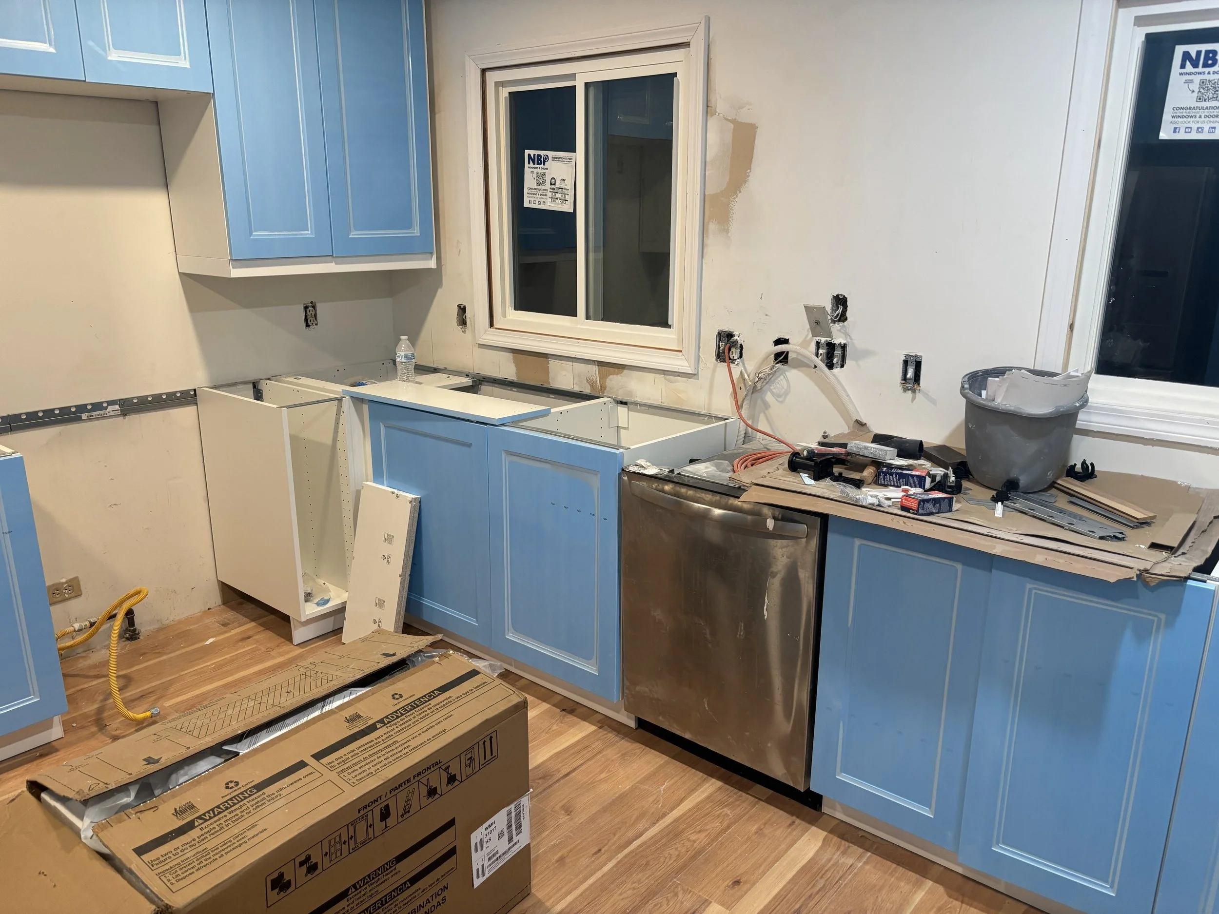 Kitchen under renovation with incomplete blue cabinets, counter space, and tools on countertop.