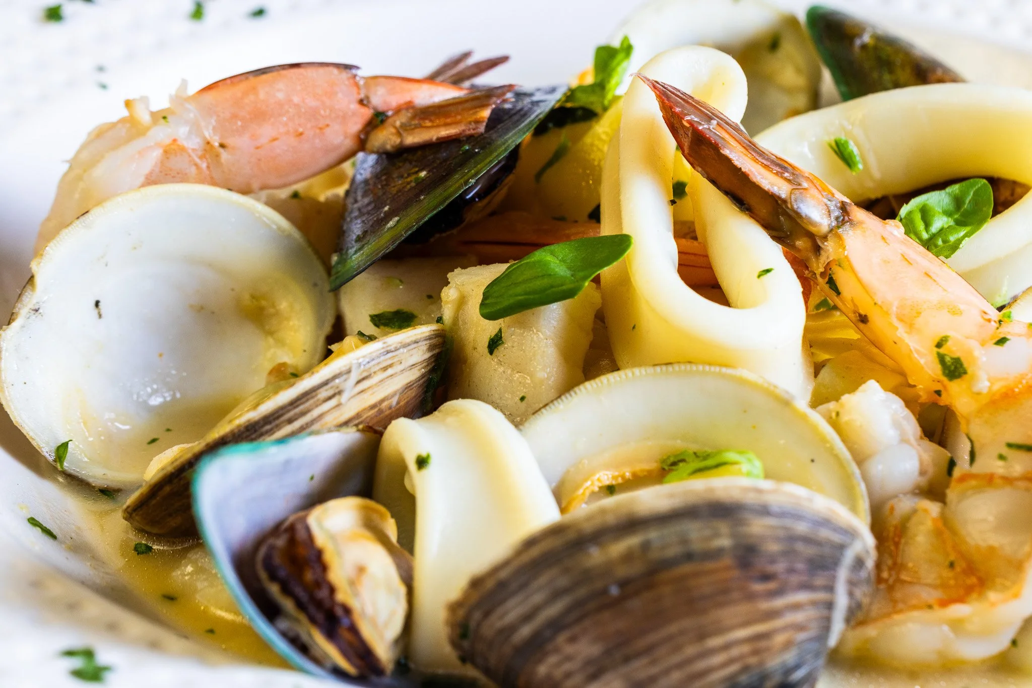 Seafood pasta dish with shrimp, clams, mussels, and squid garnished with herbs.