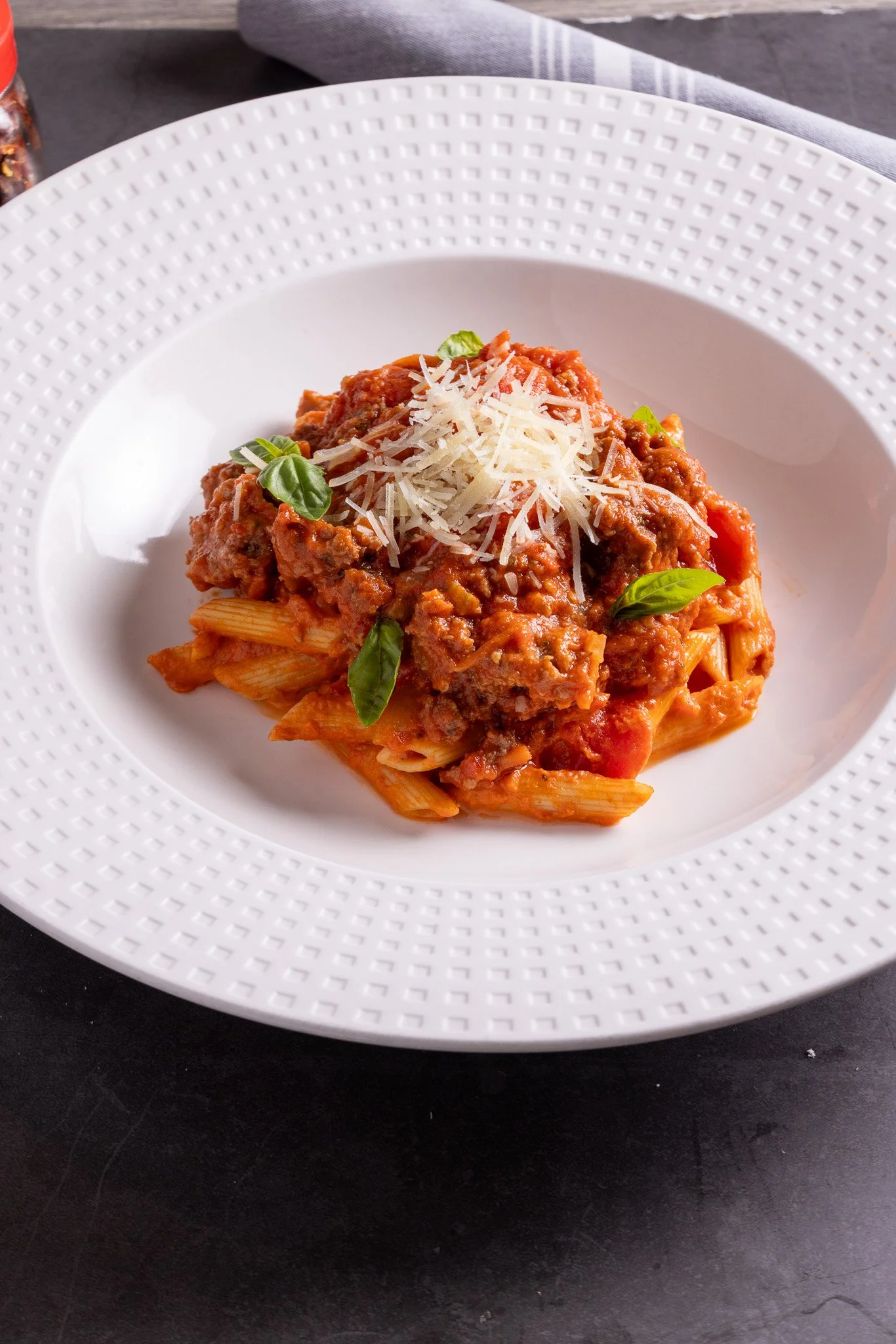 Plate of pasta with meat sauce, topped with shredded cheese and fresh basil leaves.