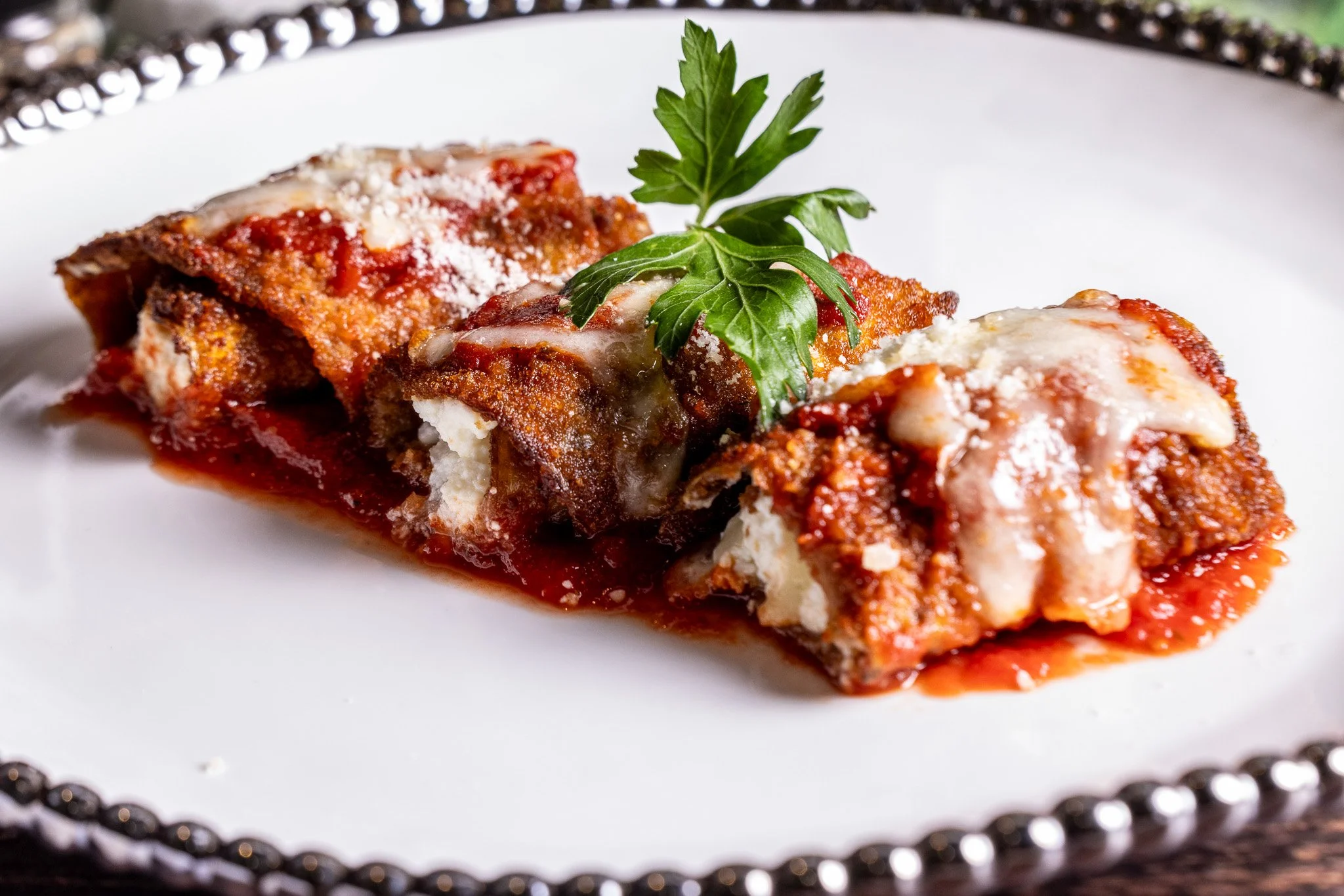 Slice of lasagna with melted cheese, tomato sauce, garnished with fresh parsley on a white plate.