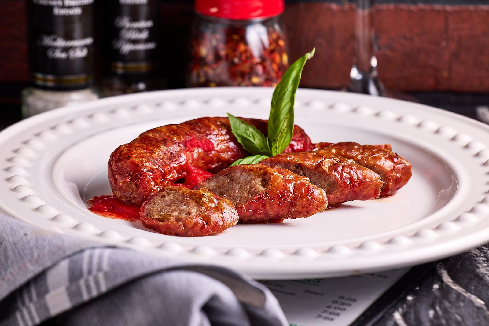 Cooked sausage on white plate garnished with fresh basil leaves.