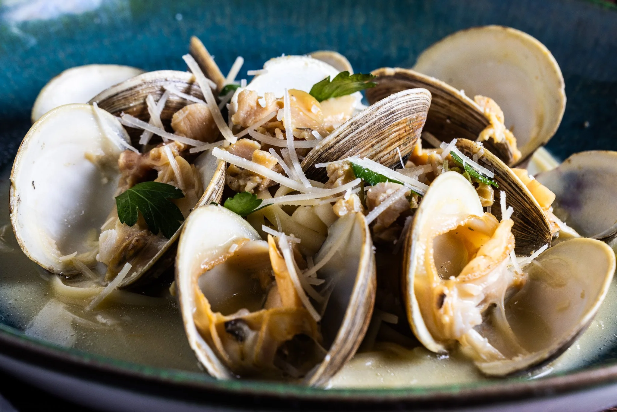 Clam pasta dish with clams, grated cheese, herbs, and pasta in a broth.