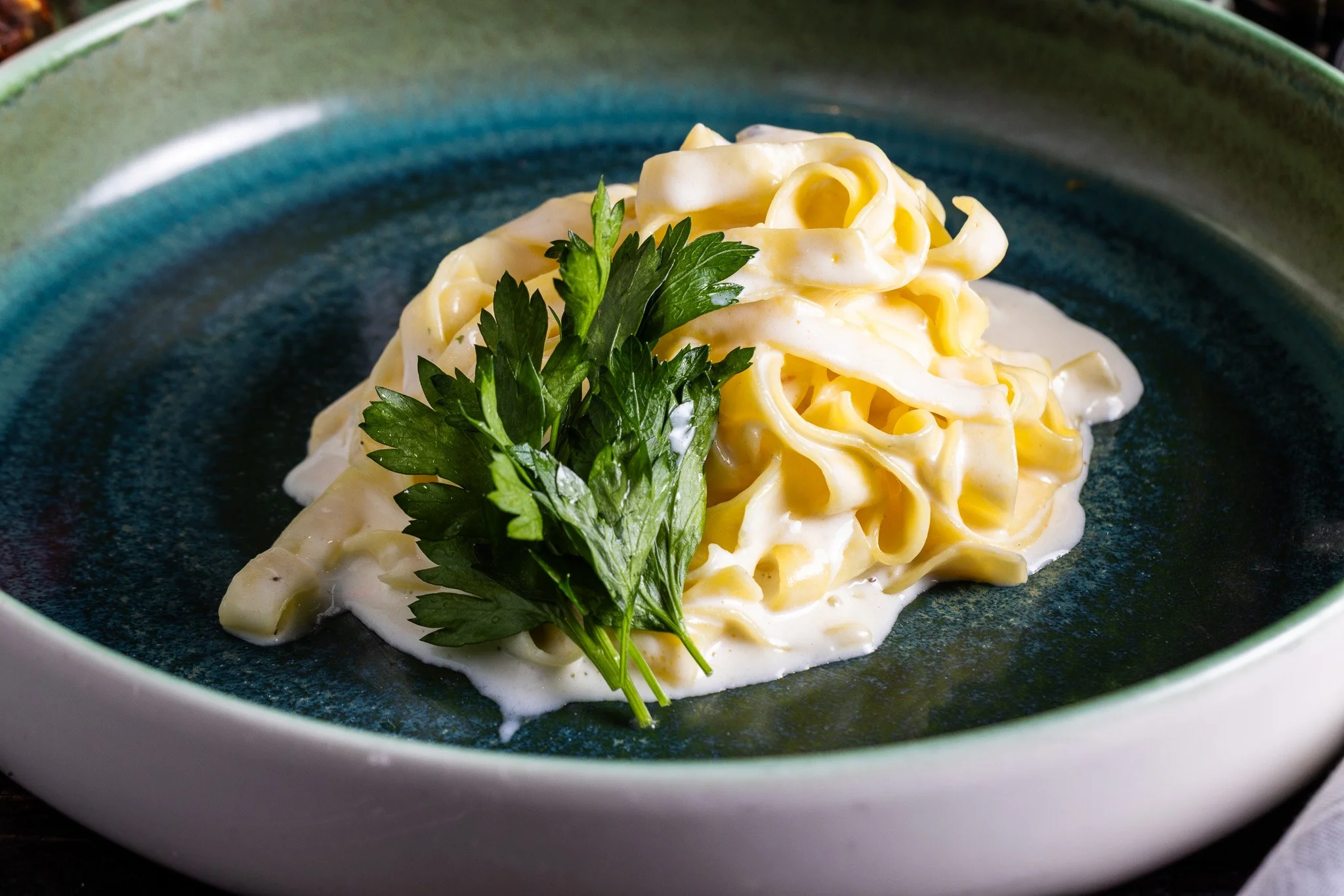 Fettuccine pasta with creamy white sauce and garnished with parsley on a dark green plate.