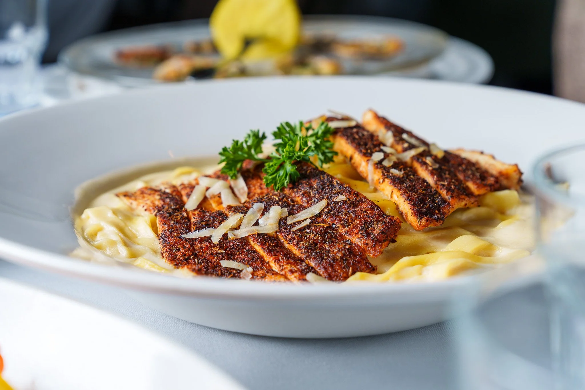 A plate of creamy pasta topped with grilled salmon fillet garnished with parsley and shredded cheese.
