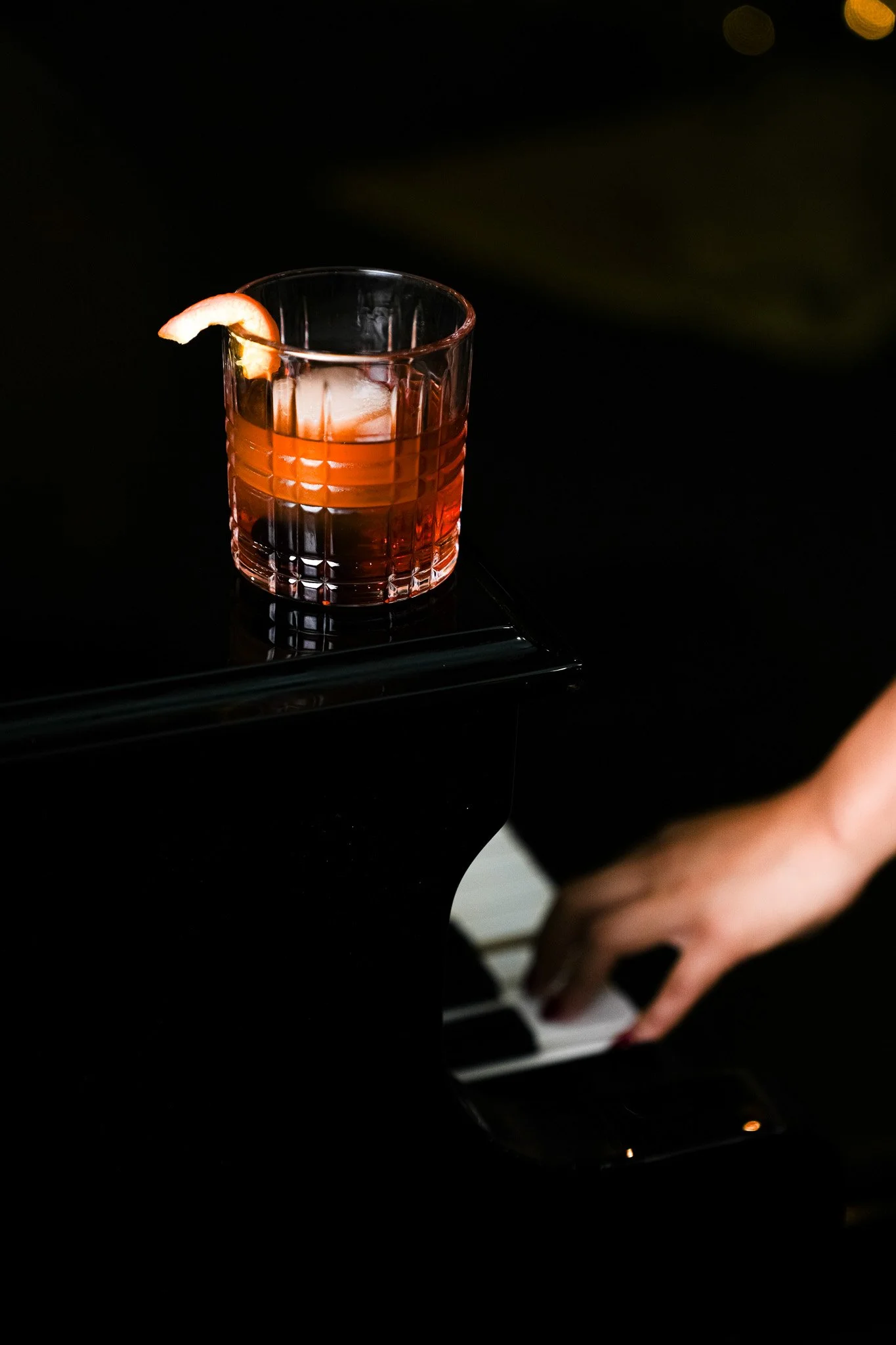A glass of cocktail with an orange slice garnish on a piano.