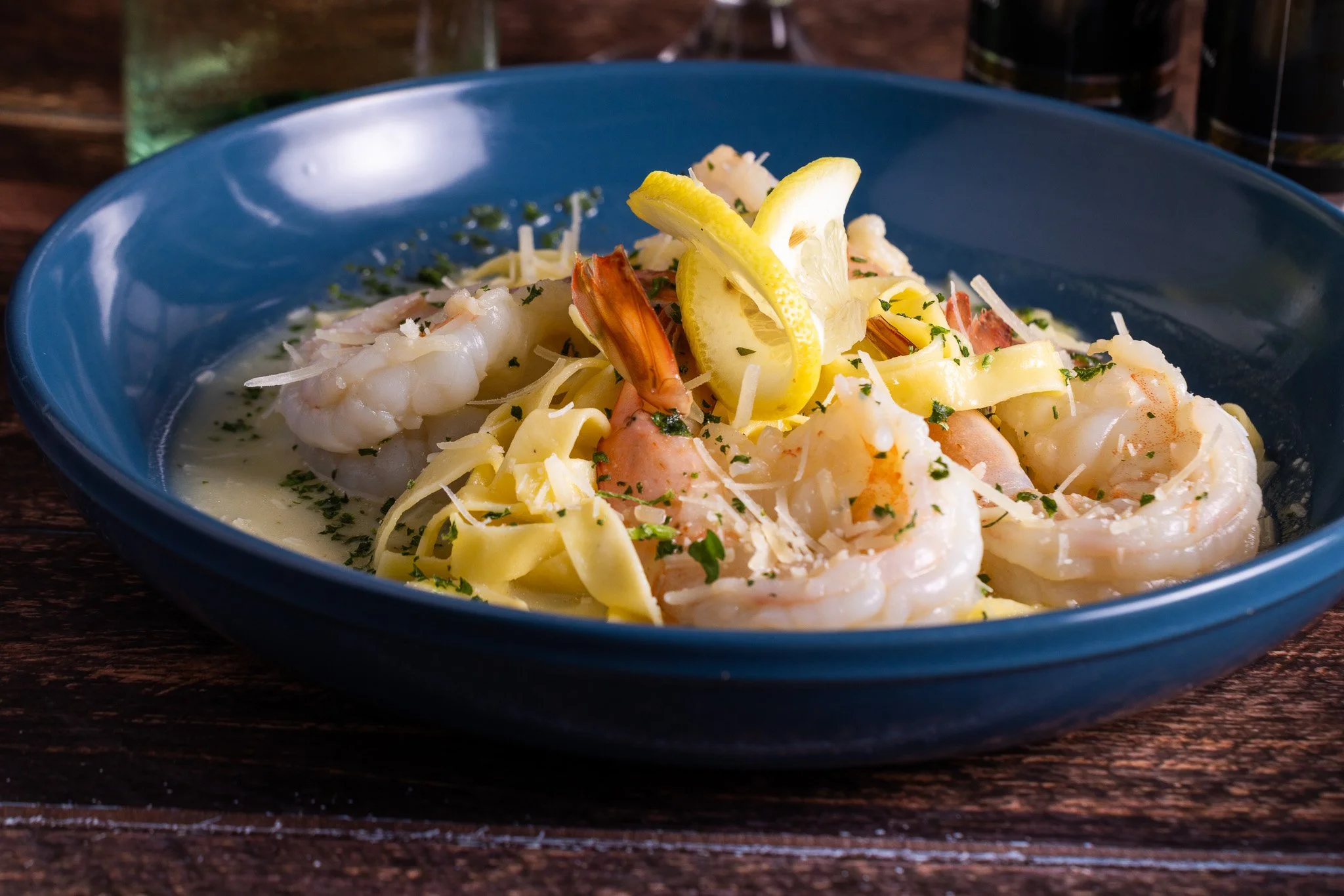 A blue bowl of creamy shrimp Alfredo pasta garnished with lemon slices and herbs.