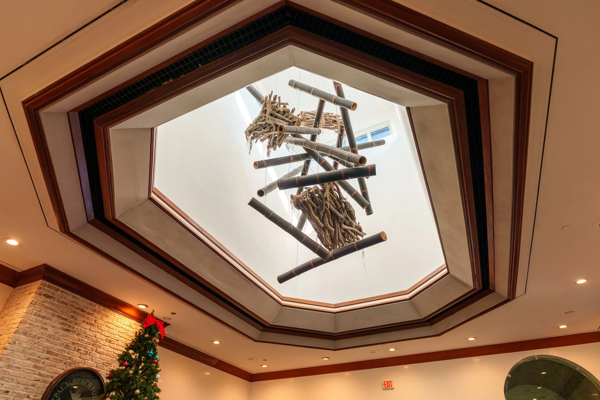 Decorative hanging sculpture made of bamboo poles and driftwood inside a building with a stained glass skylight.