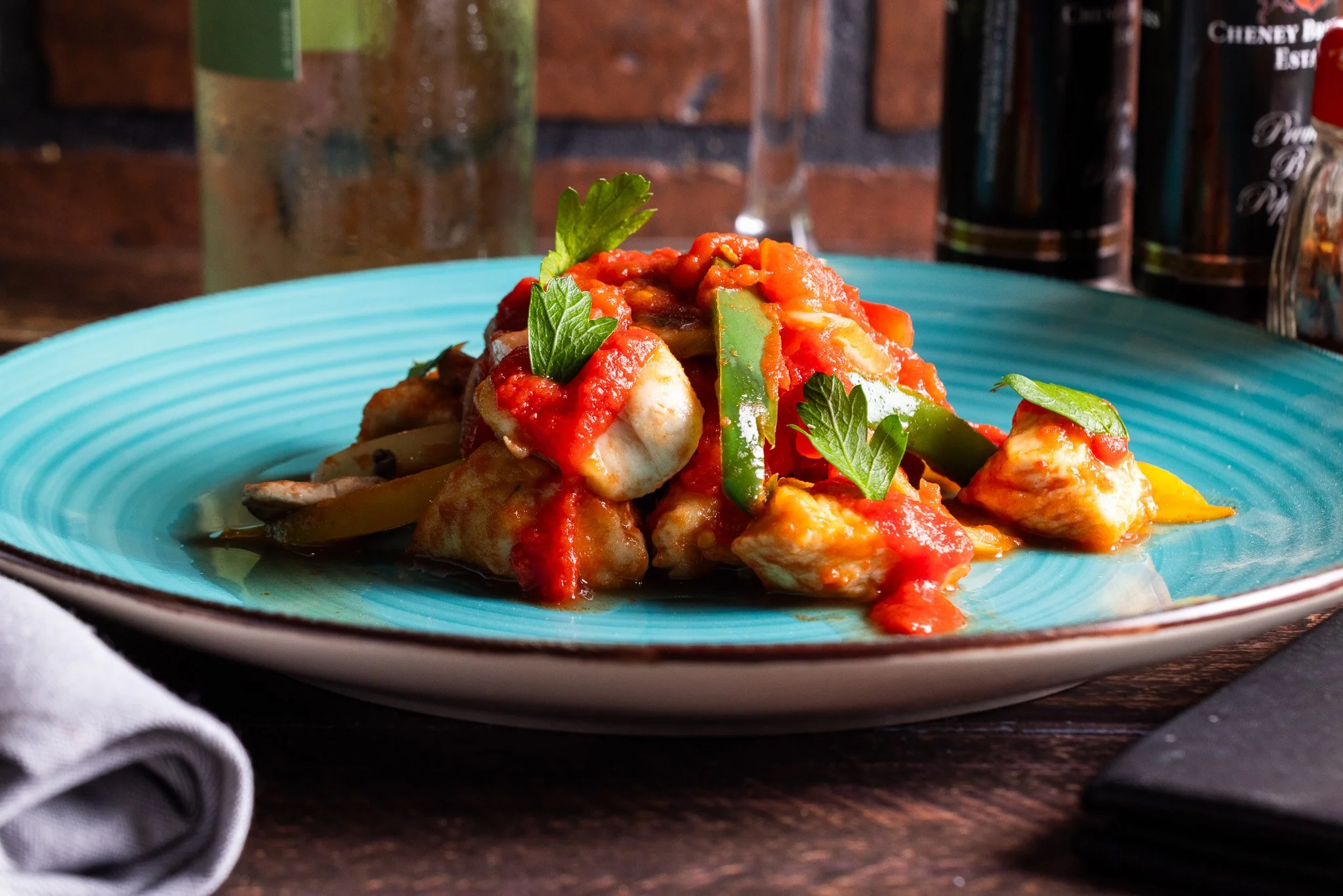Plate of chicken and vegetable stir-fry with red sauce, garnished with parsley, served on a turquoise plate.