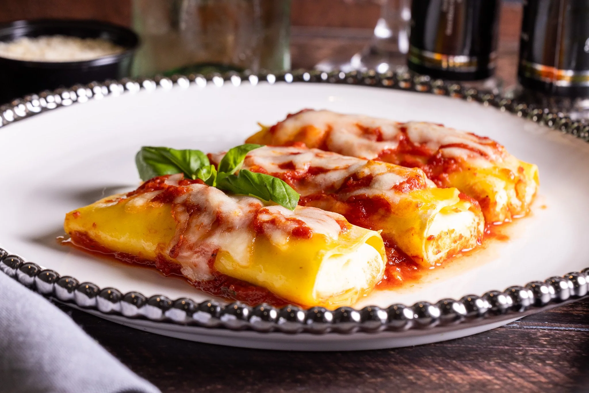 Two cheese and tomato stuffed cannelloni topped with melted cheese and basil leaves on a white plate.