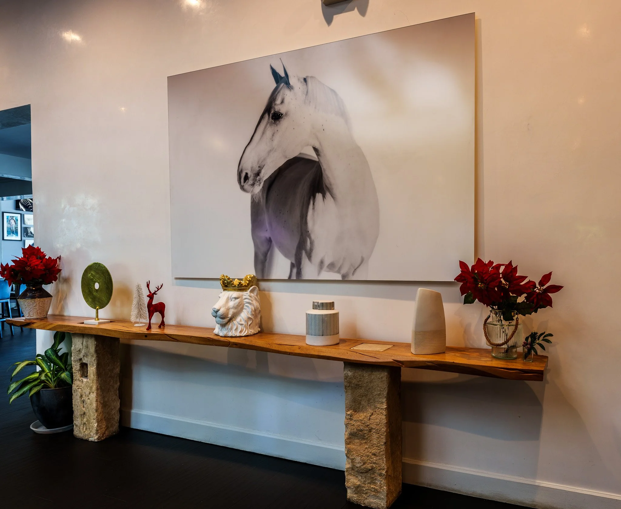 Decorative display featuring a large black-and-white painting of a horse hanging on a beige wall. The display table below has a wooden top supported by two stone blocks and is decorated with various items, including a white lion head sculpture with a