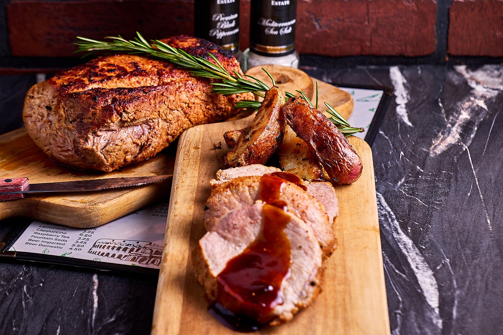Roast pork tenderloin with gravy and roasted potatoes, garnished with rosemary on a wooden serving board.