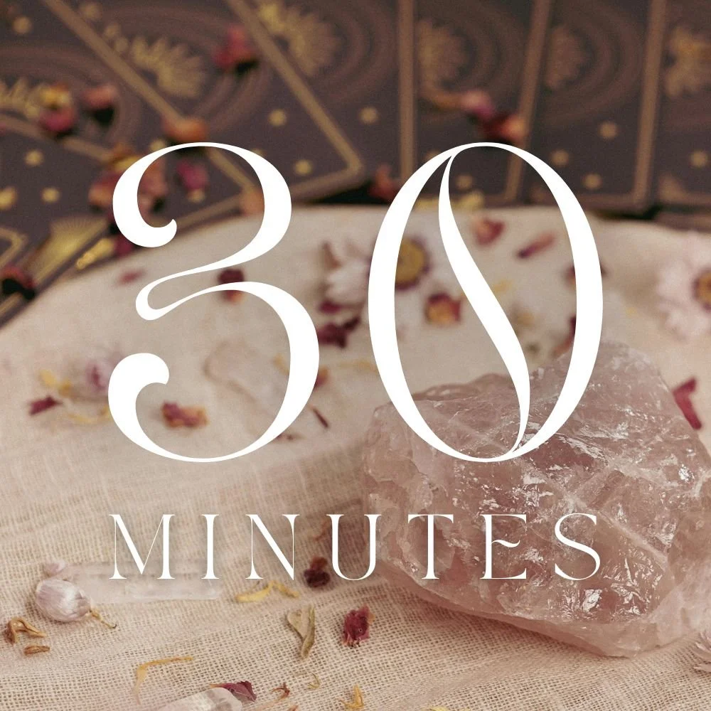 A large clear quartz crystal resting on a fabric surface with scattered flower petals, with a box of tarot cards in the background, overlaid with the text '30 Minutes' in large, elegant font.
