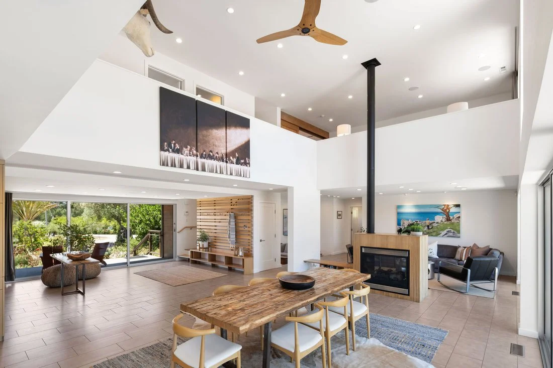 Open-concept living room and dining area with high ceilings, a ceiling fan, a fireplace, large windows, outdoor view, and modern furniture.