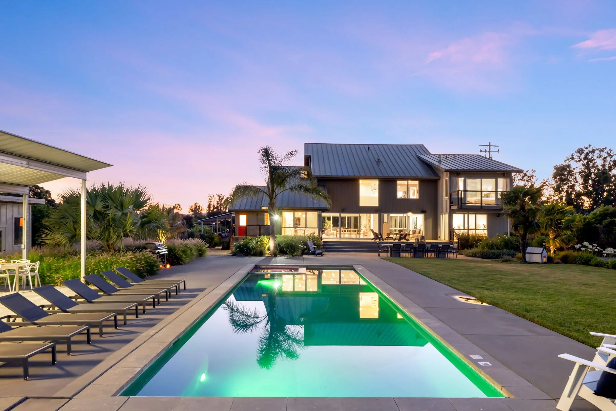 Modern house with outdoor swimming pool and lounge chairs at sunset.