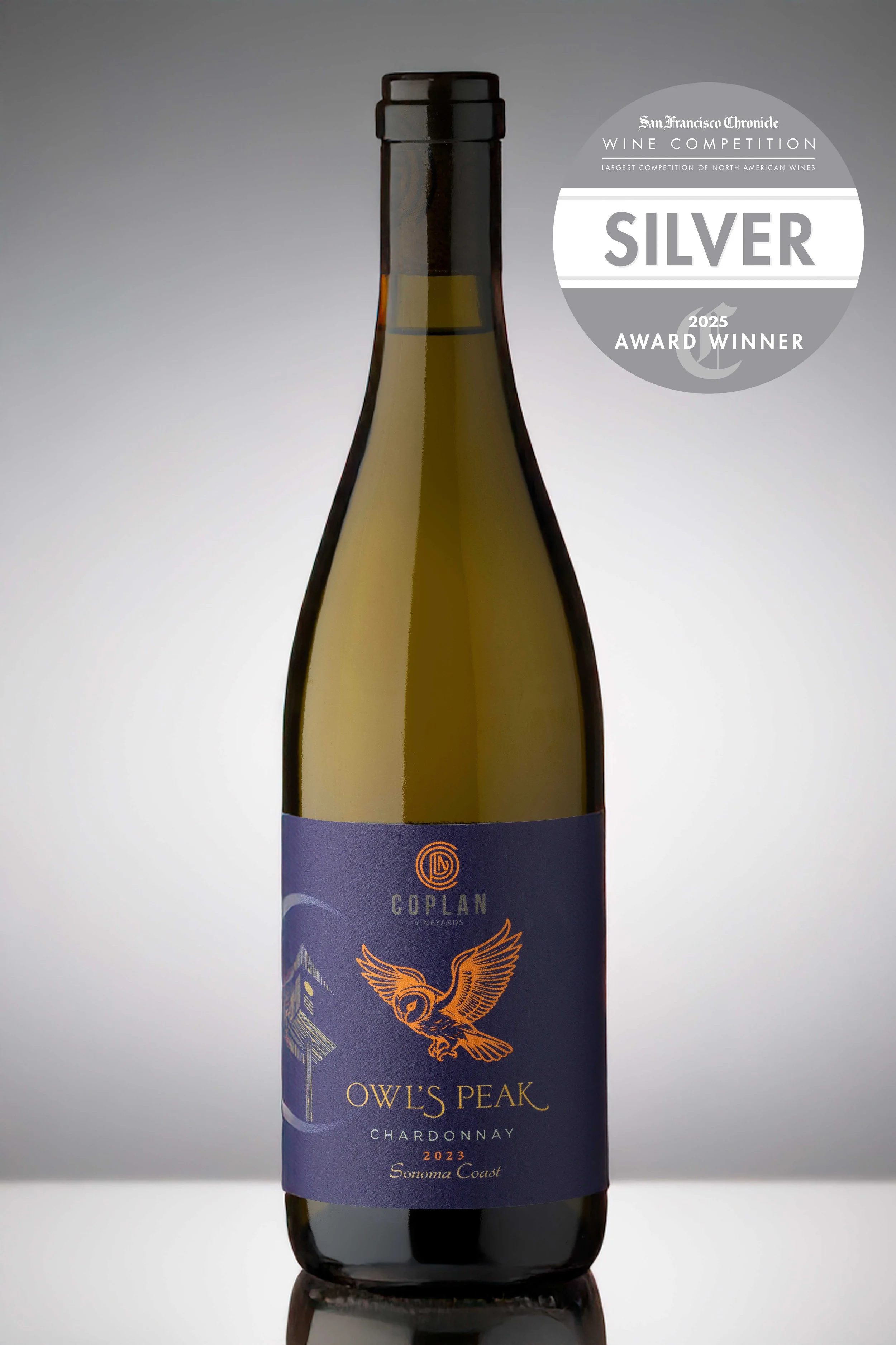 A bottle of Owls Peak Chardonnay wine with a blue label featuring an orange owl illustration, from Coplan Vineyards, vintage 2023, Sonoma Coast, with a Silver Award badge from the 2025 San Francisco Chronicle Wine Competition.