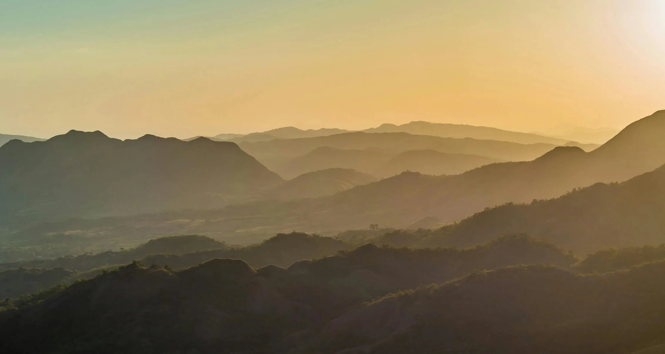 Layers of mountains during sunset with a warm yellow-orange sky.