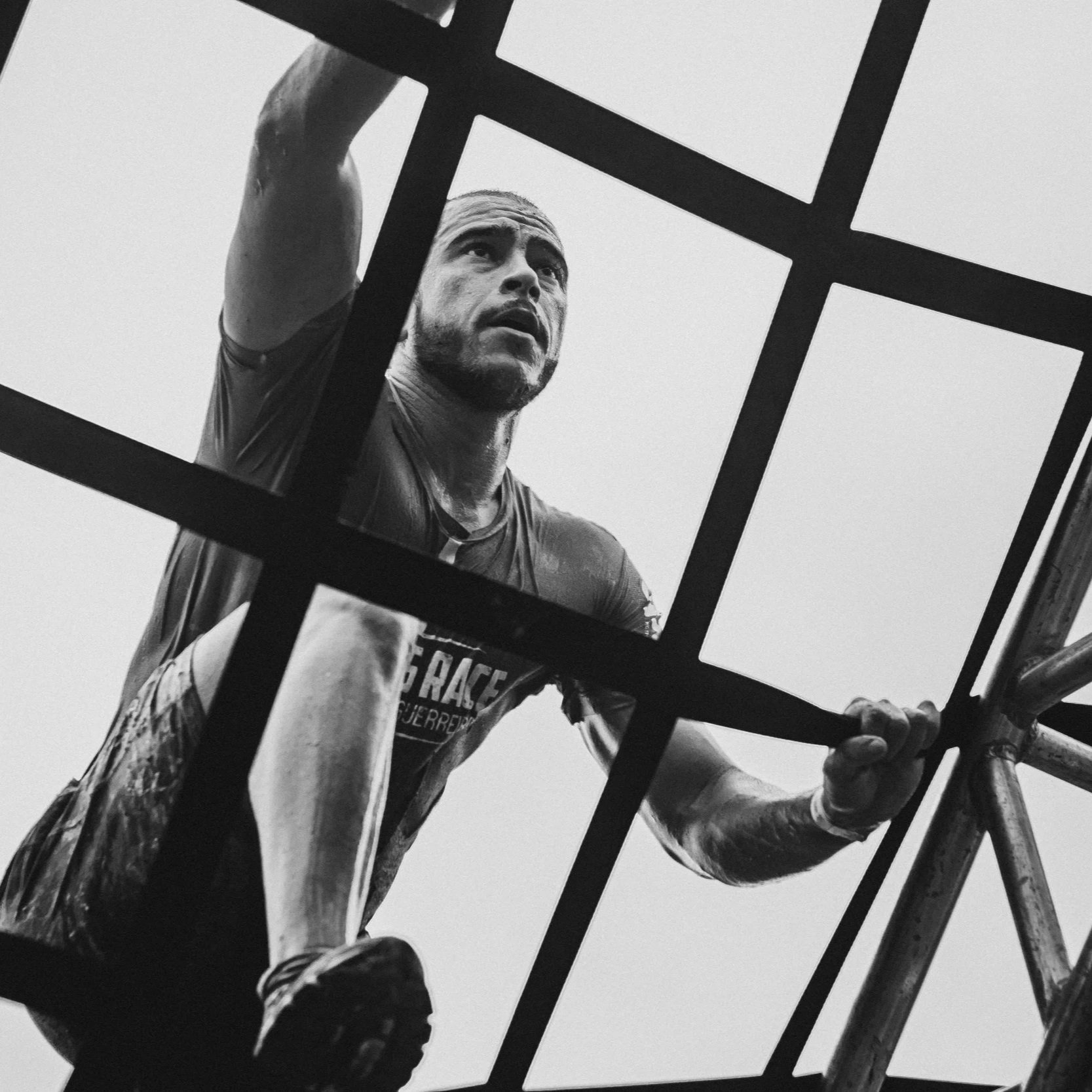 Black and white photo of a man climbing a metal structure, looking up with a serious expression.