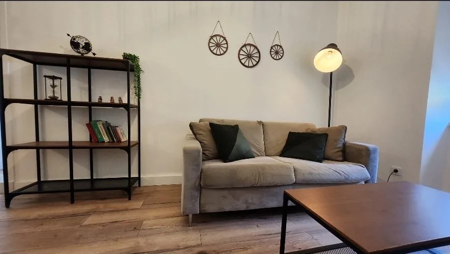 Salon avec un canapé beige, une étagère en bois noir, un lampadaire à lampes rondes, une table en bois, et une décoration murale avec trois roues en fer suspendues.