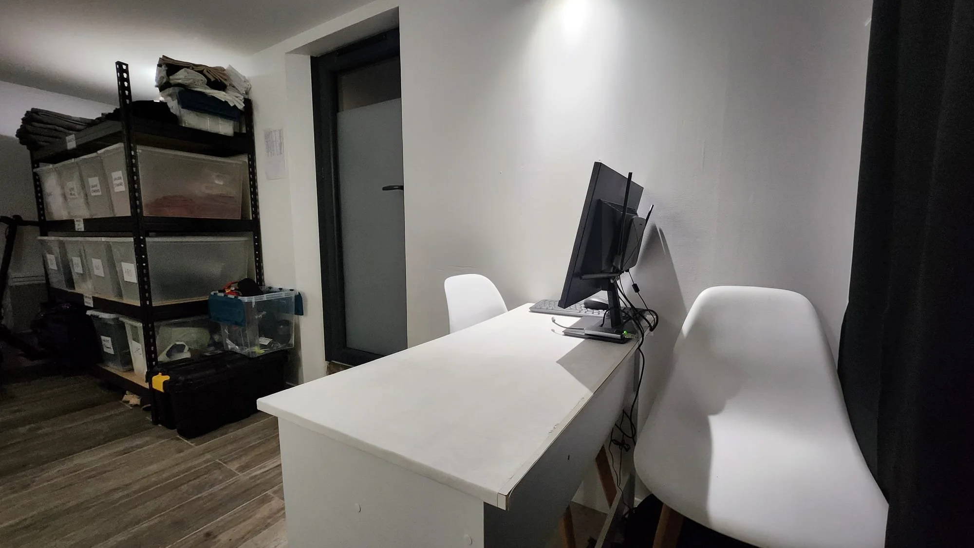 Bureau avec ordinateur, meuble de rangement noir avec dossiers et boîtes transparentes, et deux chaises blanches.