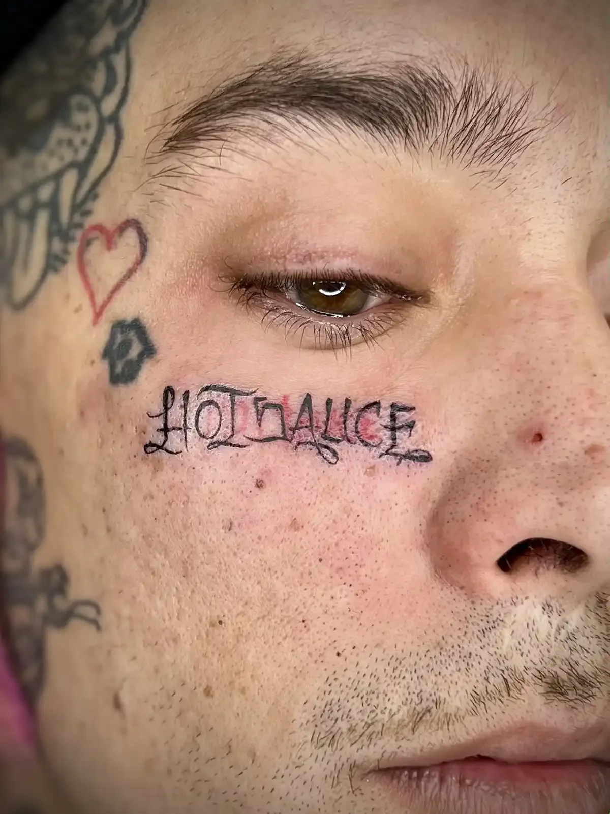 Face tattoos with red heart, black mask, and Loyalty lettering under the eye by Austin tattoo artist Johny Vasquez - Mommasboy Tattoo