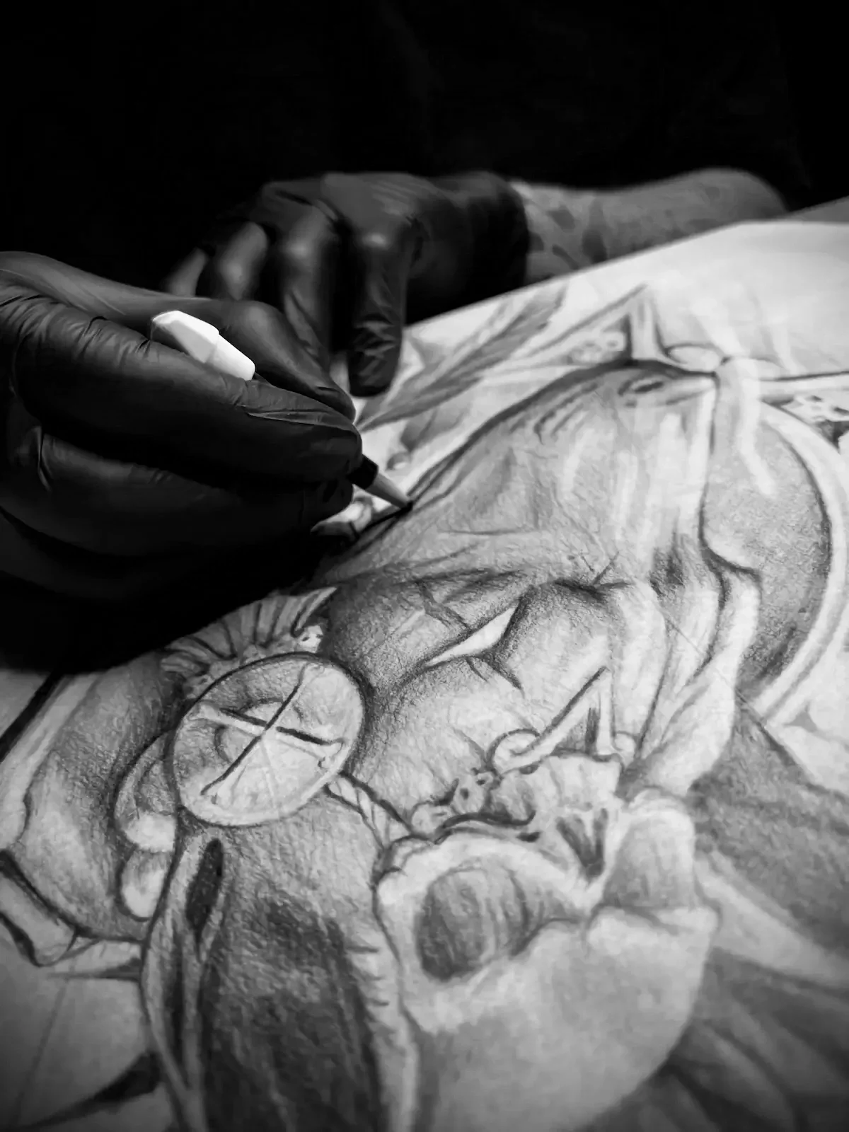 Austin tattoo artist Mommasboy Tattoo in black gloves sketching a detailed tattoo of a face on a person's arm with a marker.