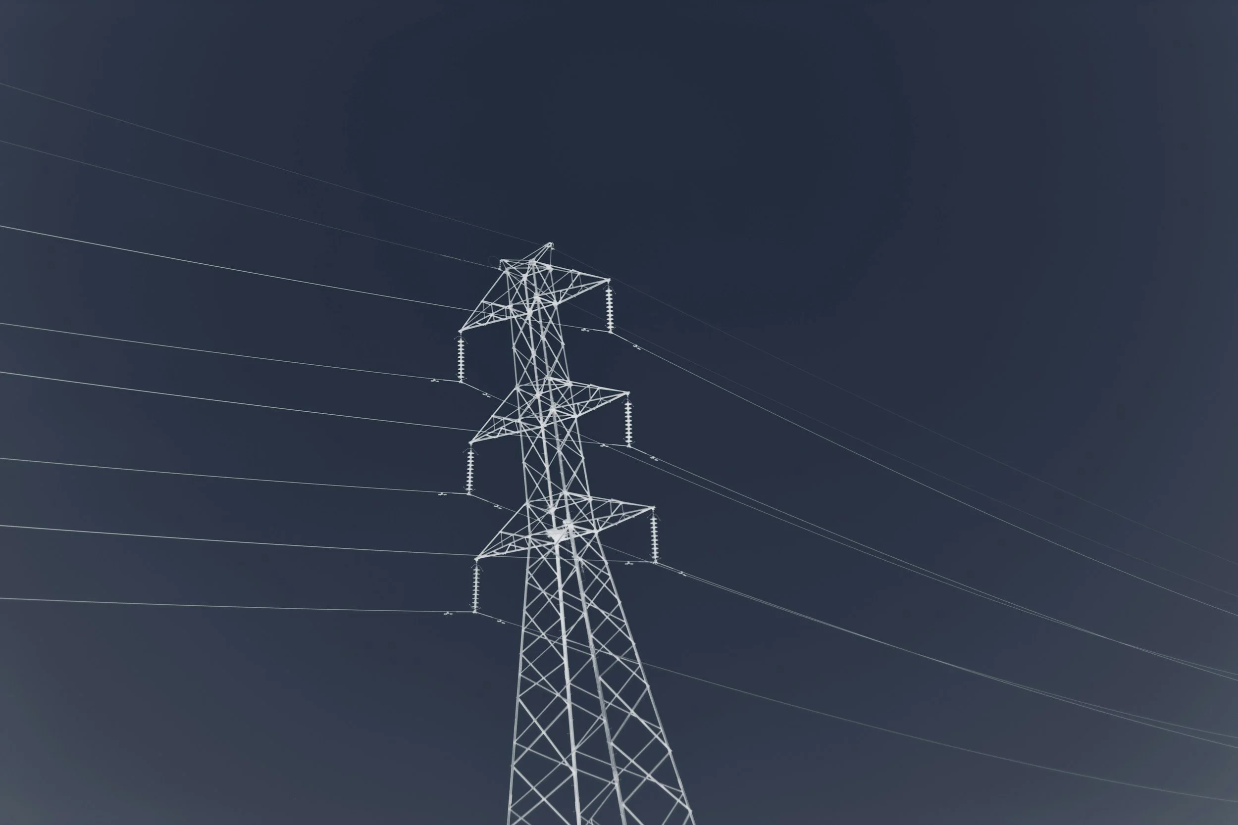 An electrical transmission tower with power lines against a dark sky.