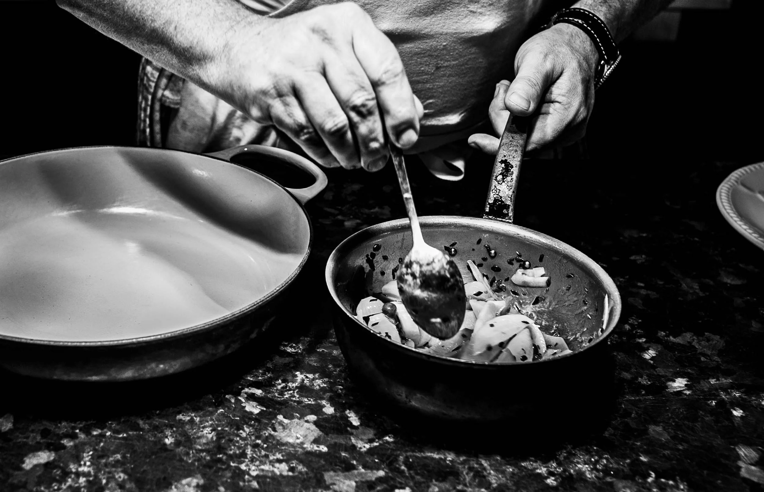 Person serving food from a metal pot into a bowl on a dark countertop.