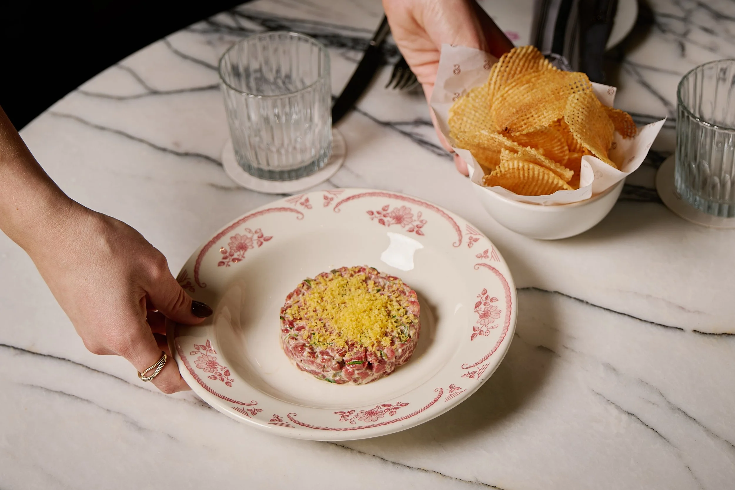 A person presenting a plate of beef tartare.