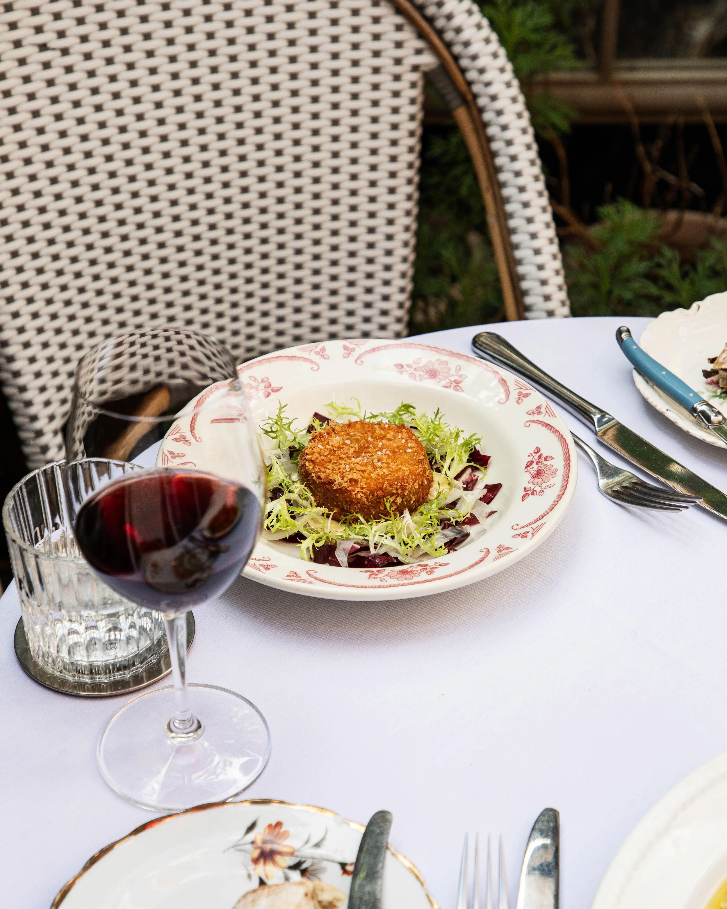 Close-up of a table setting with a glass of red wine, a plate of food, and silverware, on a white tablecloth.