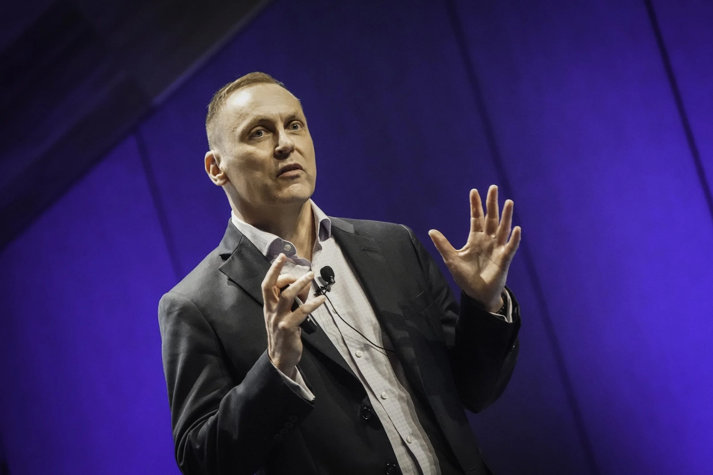 Photo of Damian Green giving a presentation on a stage with a purple background.