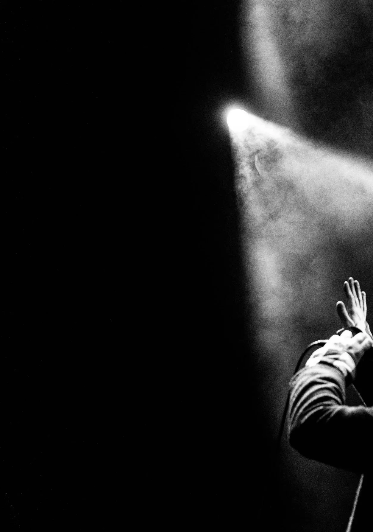 A person with a striped sleeve reaching out with their hand toward a bright light beam in a dark environment, creating a dramatic contrast.