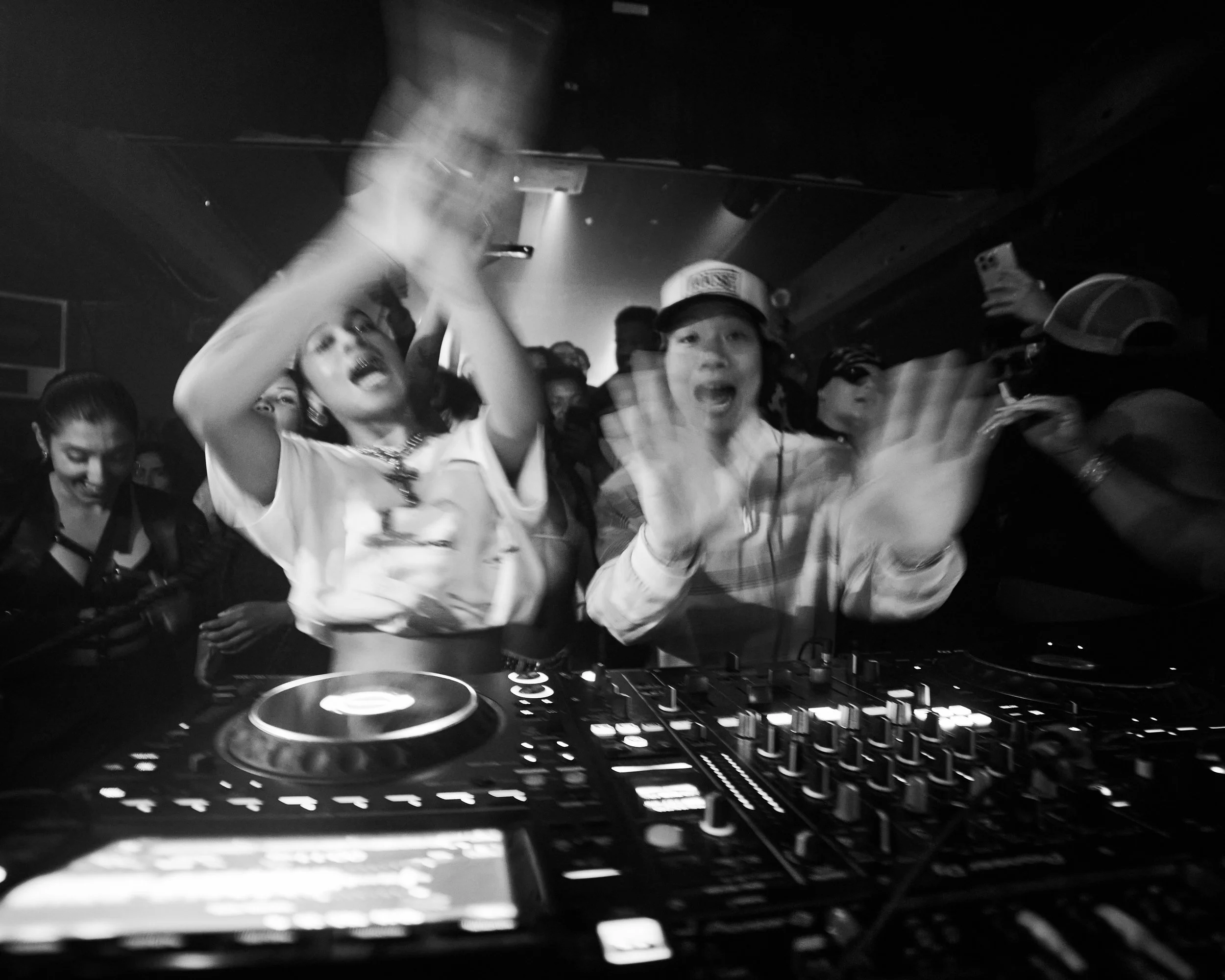 People dancing and partying at a nightclub, with a DJ playing music on a turntable in the foreground.