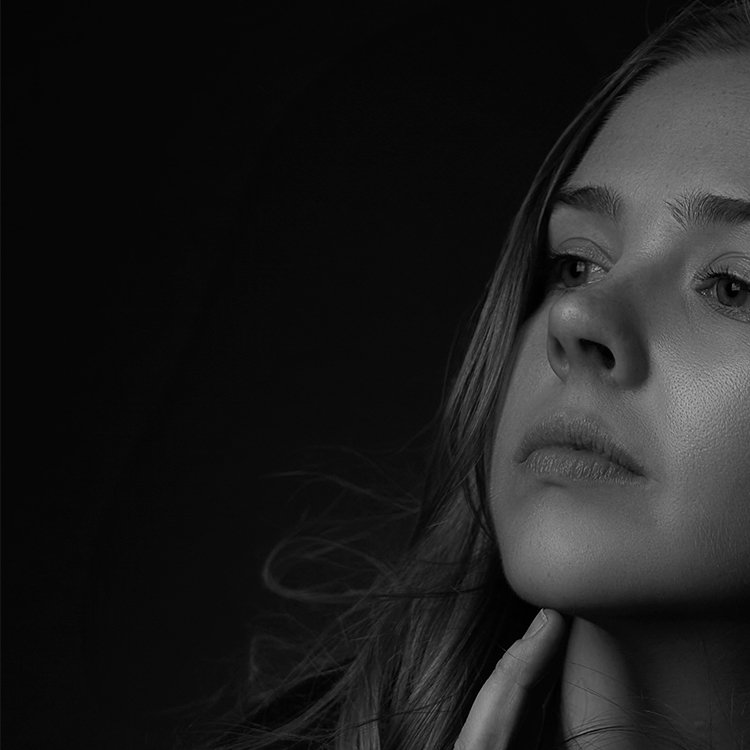 A black and white close-up portrait of a young woman with long hair, looking contemplative against a dark background.