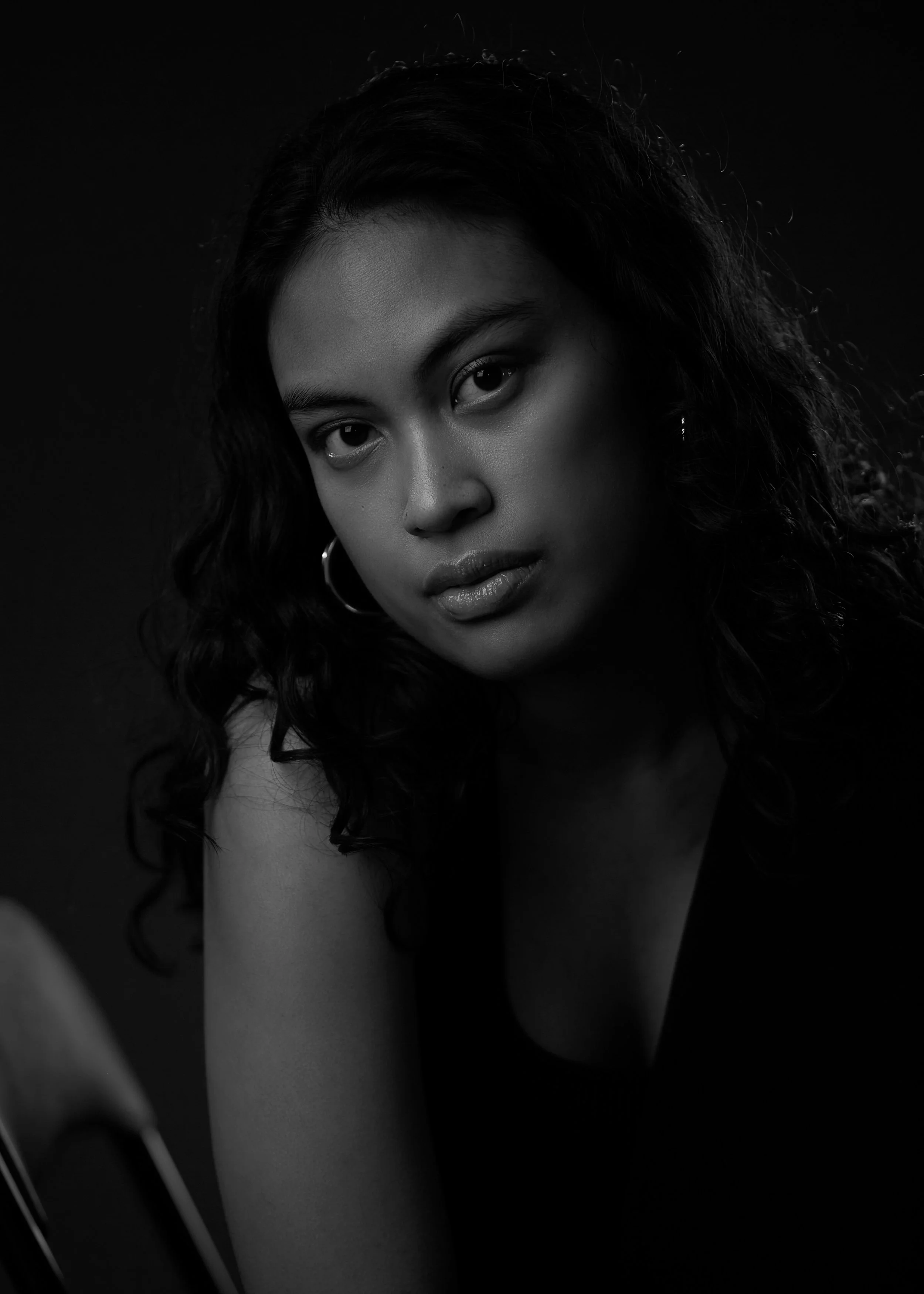 A black-and-white portrait of a woman with curly hair, wearing hoop earrings, looking directly at the camera with a serious expression.