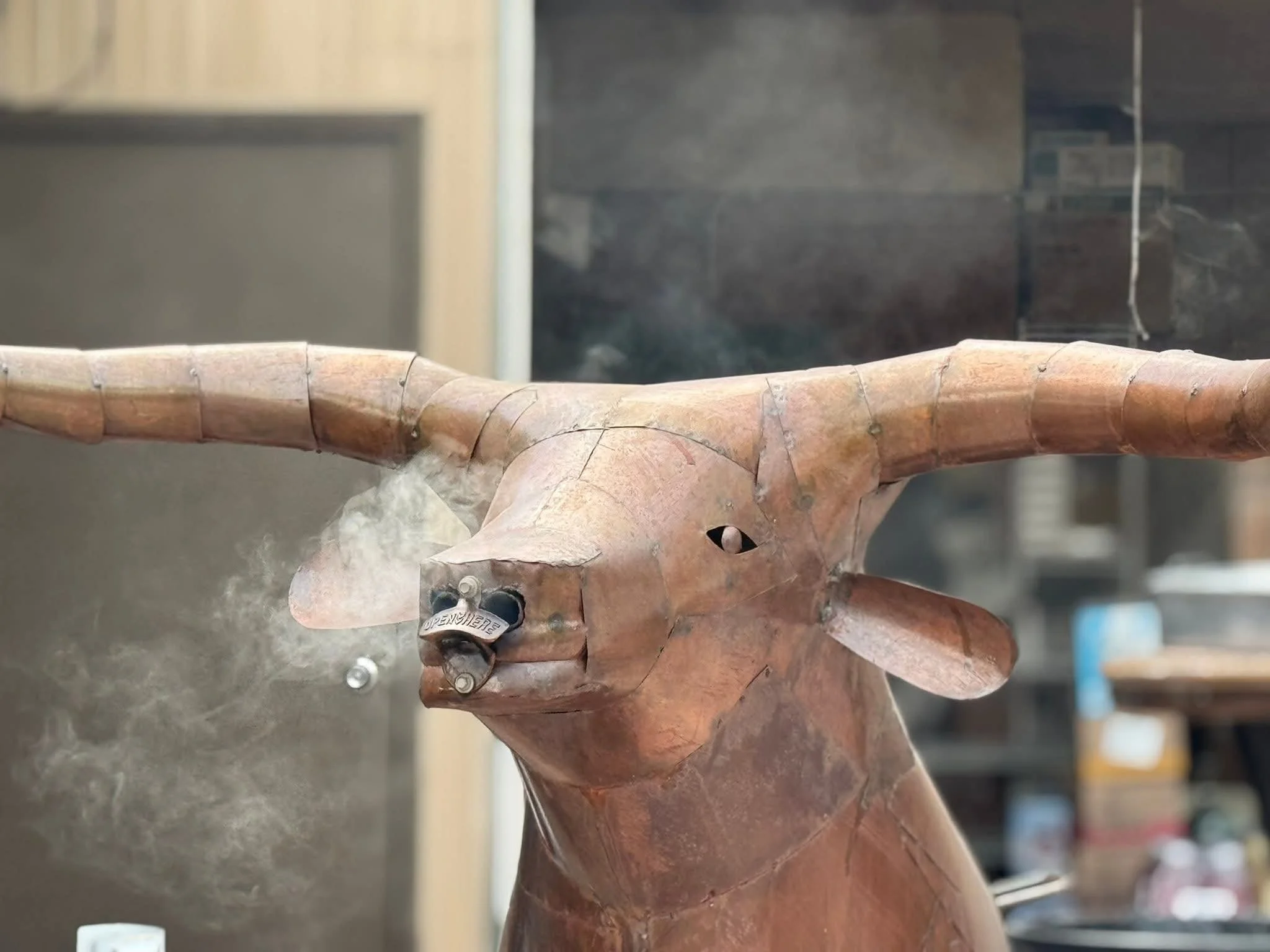 A wooden sculpture of a deer with steam or smoke rising from its nose, placed inside a workshop or storage area.