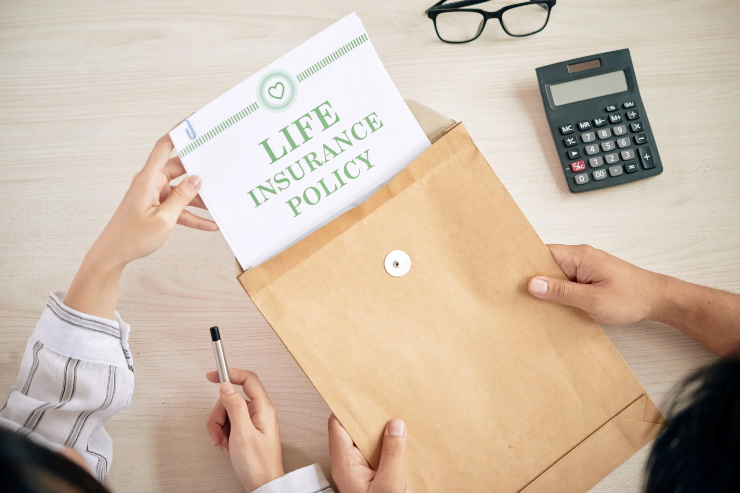 People reviewing a life insurance policy document in an office setting with a calculator and glasses on the desk.