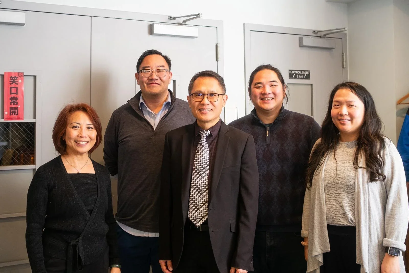 Five Chinese individuals in a group photo in front of doors
