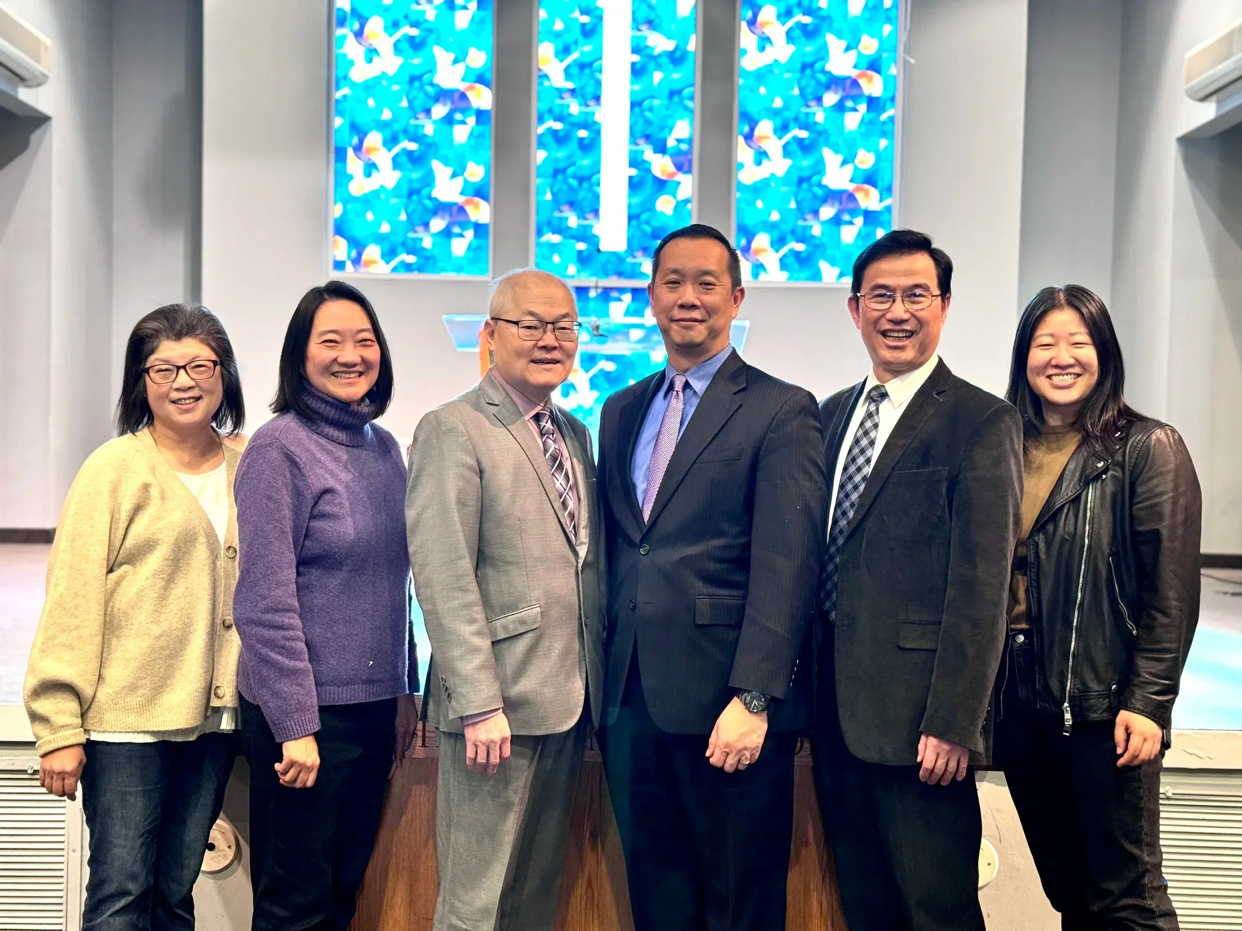 Five individuals standing at the front of a church sanctuary in front of stained glass