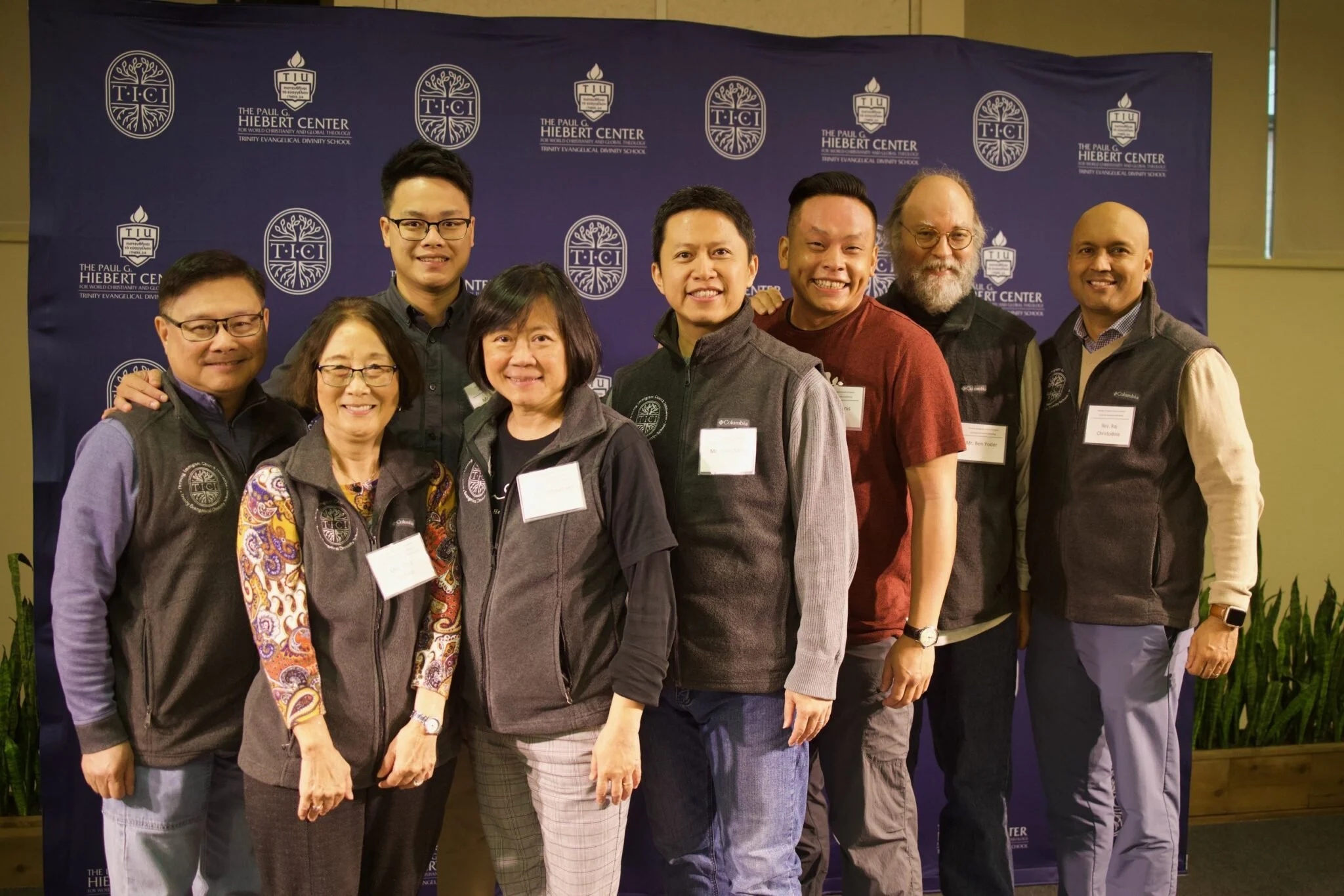 Six Chinese individuals, one caucasian individual and one Indian individual standing in front of a blue background with lettering
