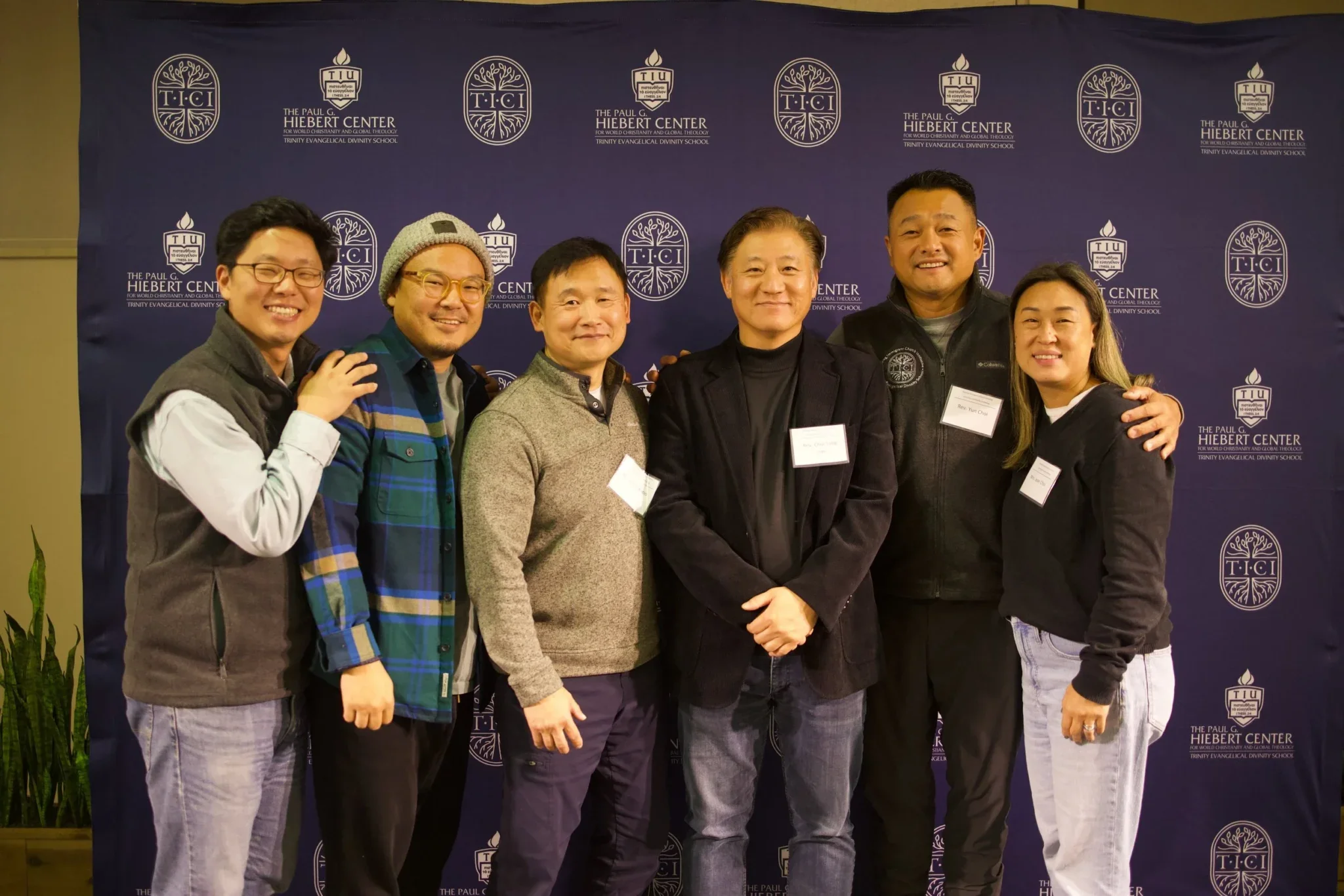 Six Korean individuals in front of a blue backddrop with white lettering