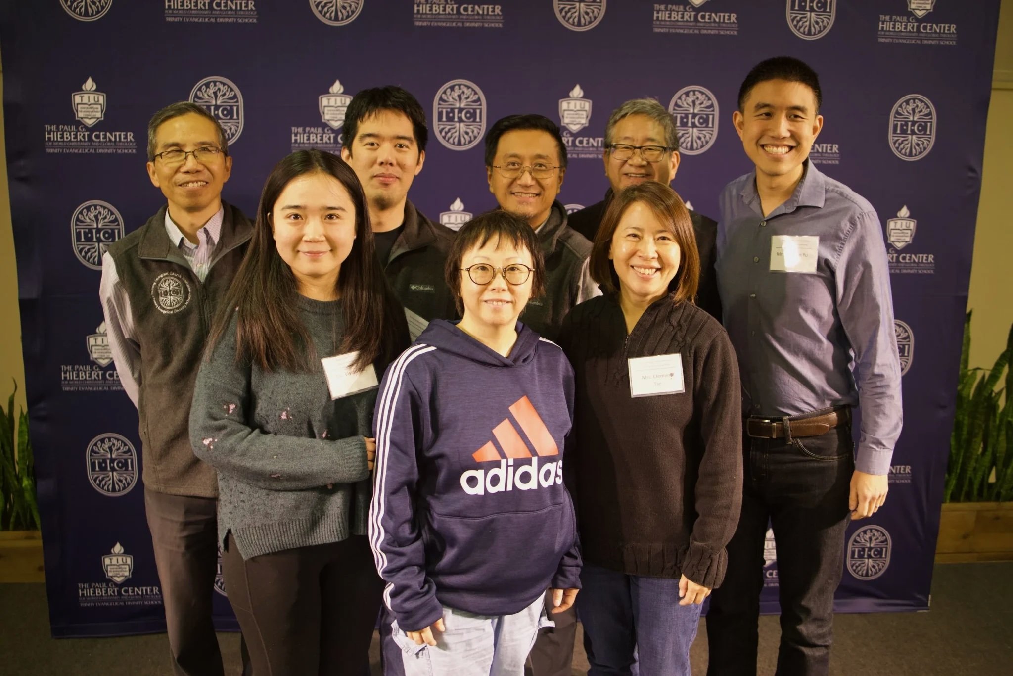 Eight individuals standing for a group photo in front of a blue backdrop with white lettering