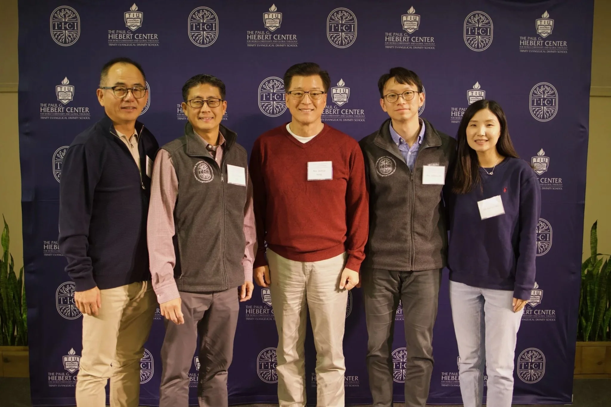 Five individuals in a group photo standing in front of a blue background with white lettering