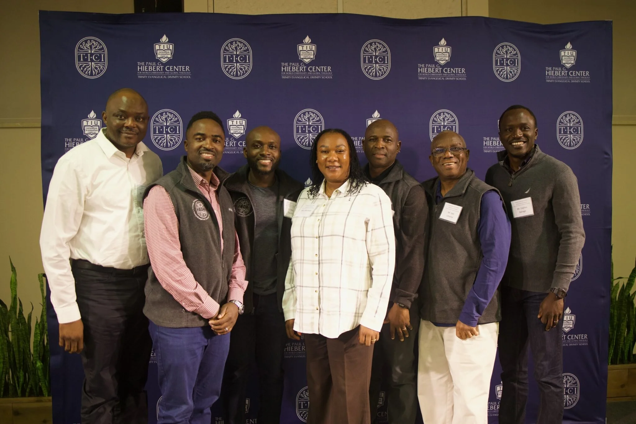 Seven African Individuals in a group photo in front of a blue background with white lettering