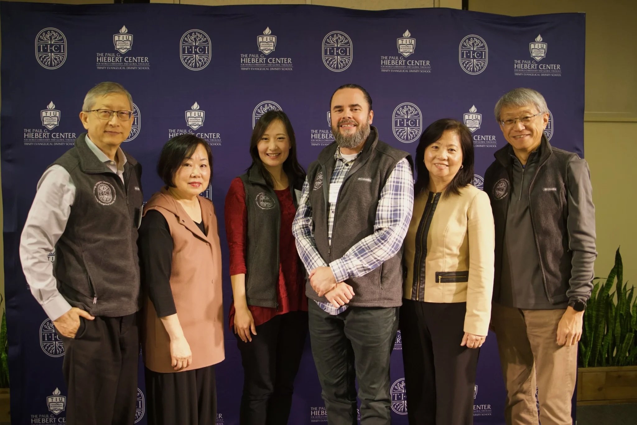 Six individuals standing for a group photo in front of a blue backdrop with white lettering