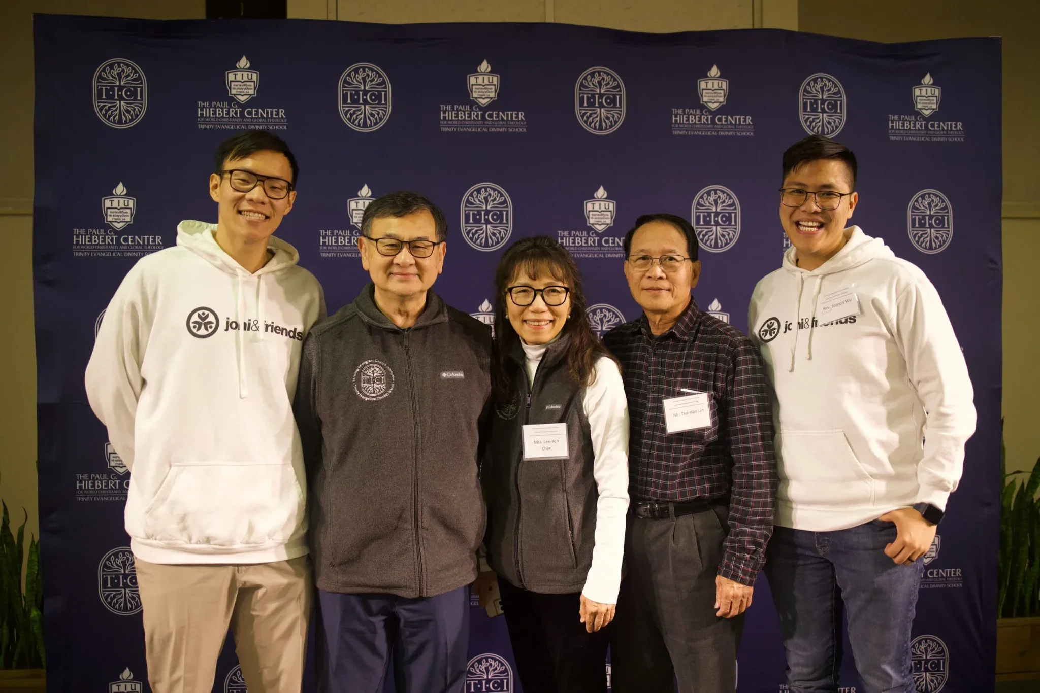 Five Chinese individuals standing in front of a blue background with lettering