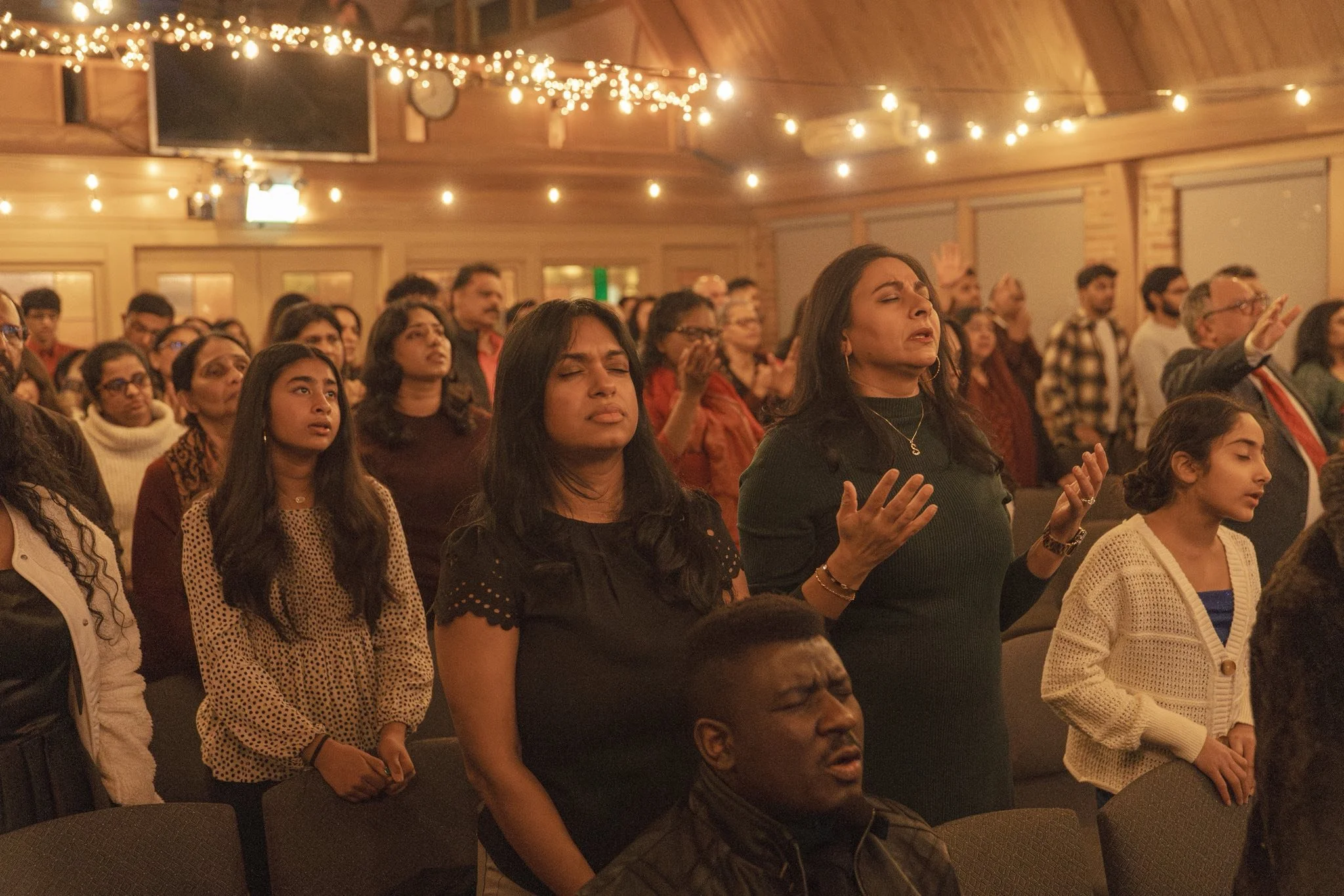 Christian church congregation worshipping together indoors with warm string lights