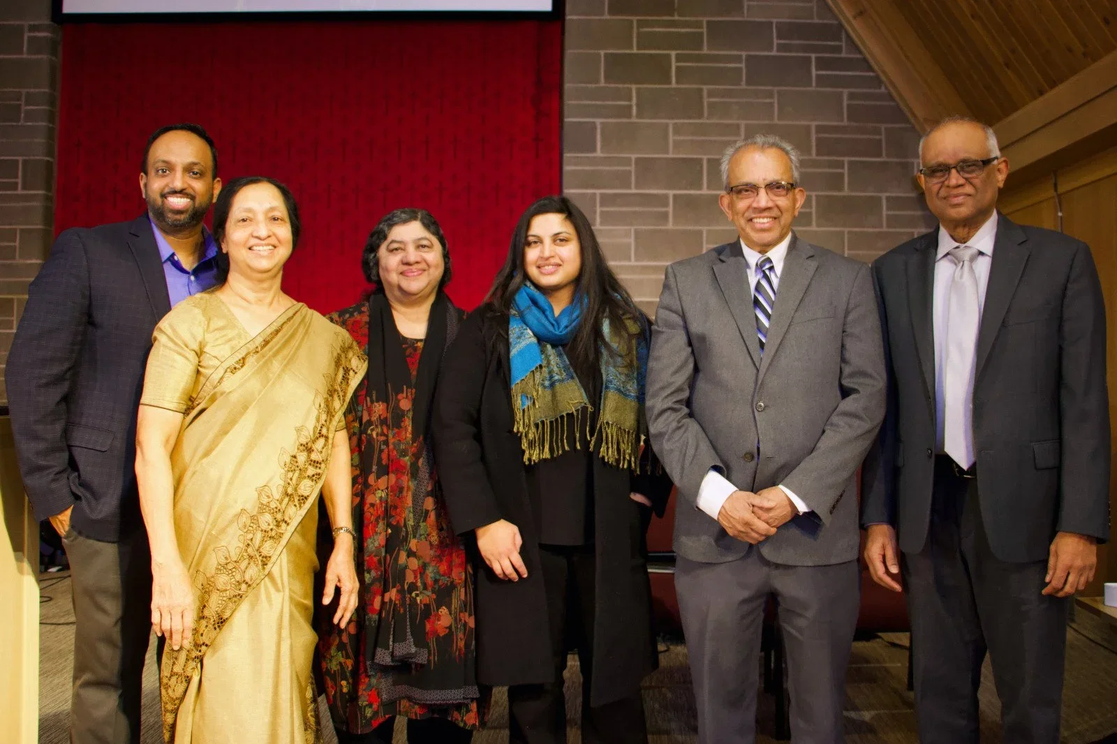 Six Indian individuals at the front of a sanctuary with cinderblock and red fabric background