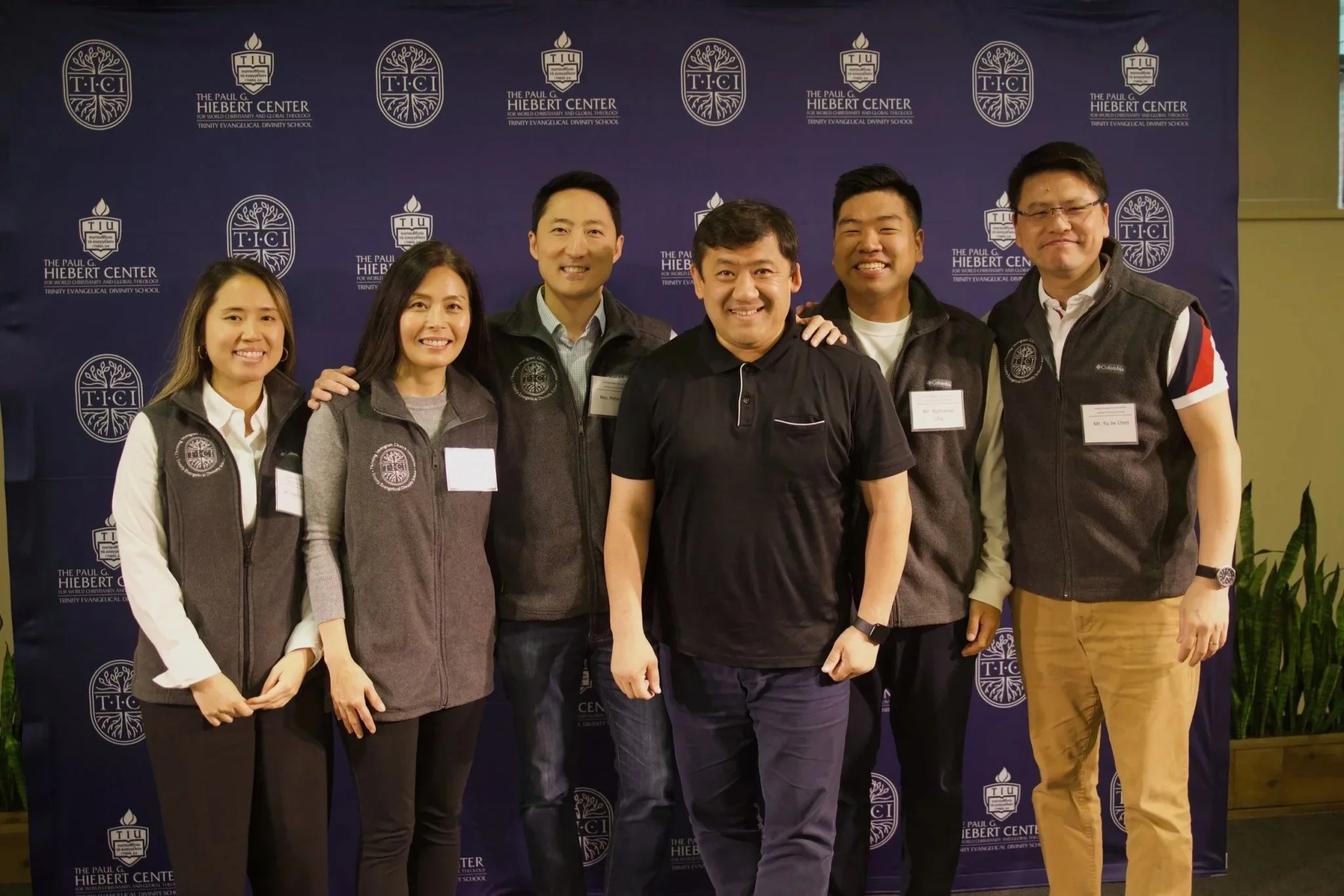 Group photo of six individuals in front of a blue background with white letters