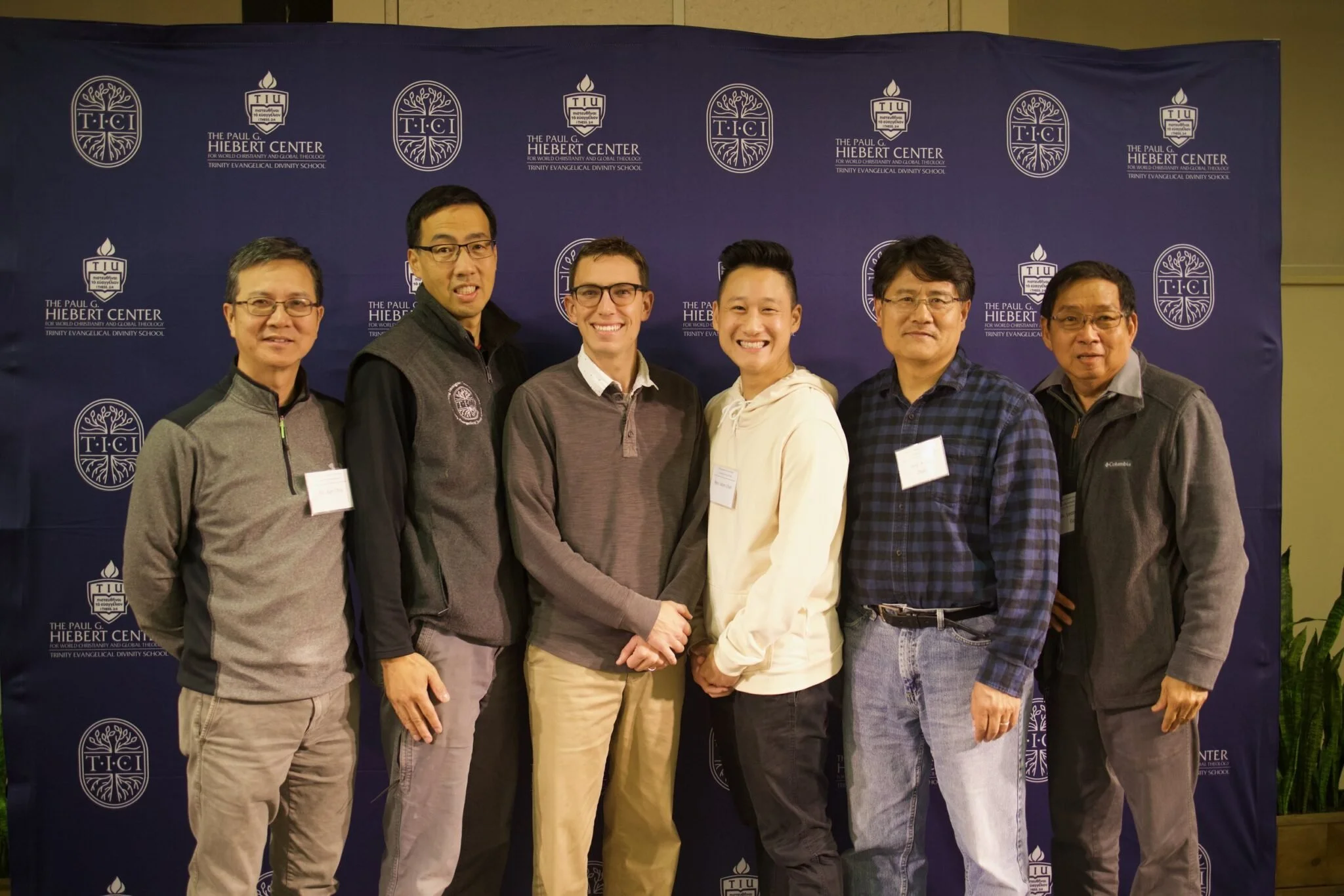 Six chinese individuals standing in front of a blue background with lettering